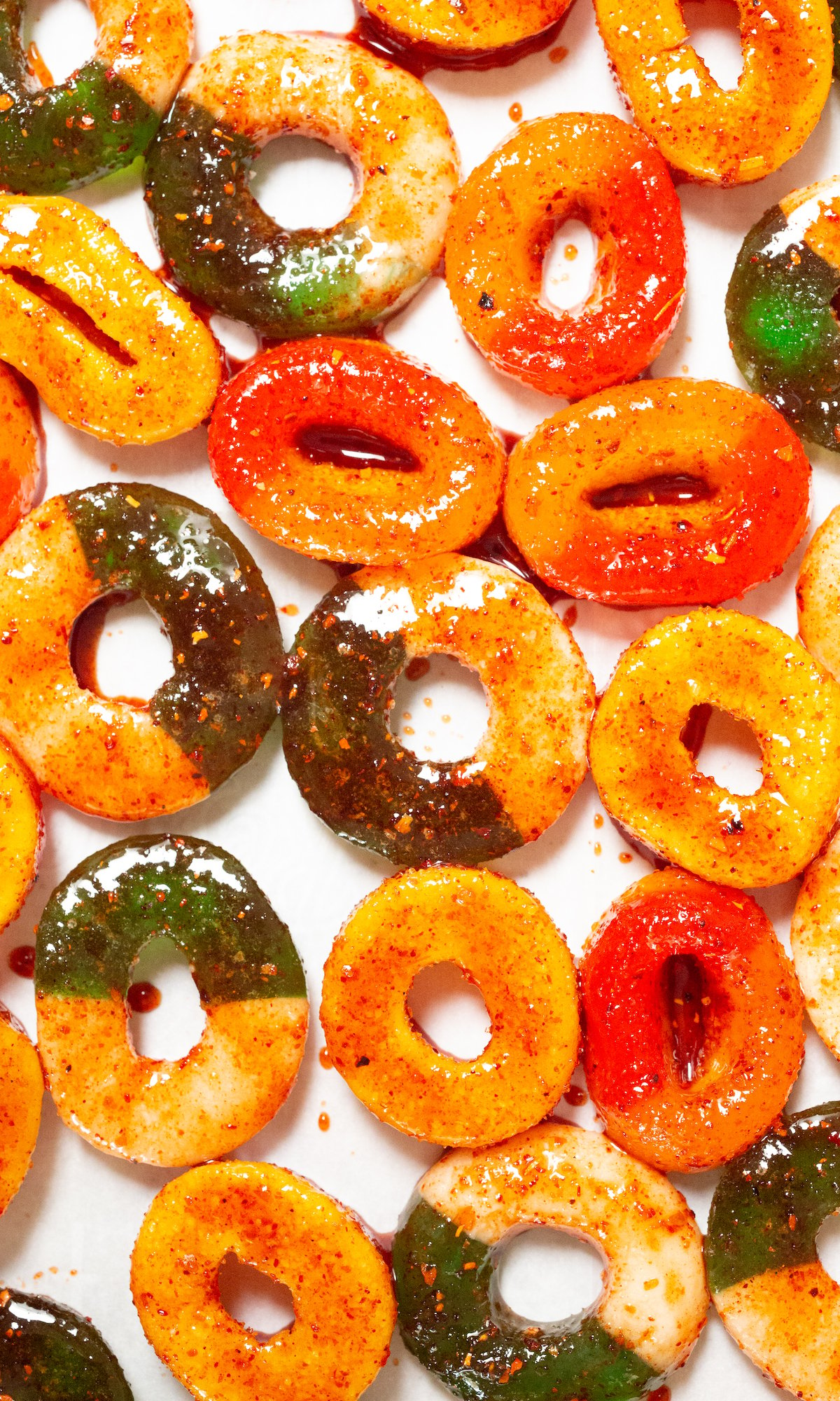 Green apple and peach gummy rings covered in Chamoy and Tajin on parchment paper.