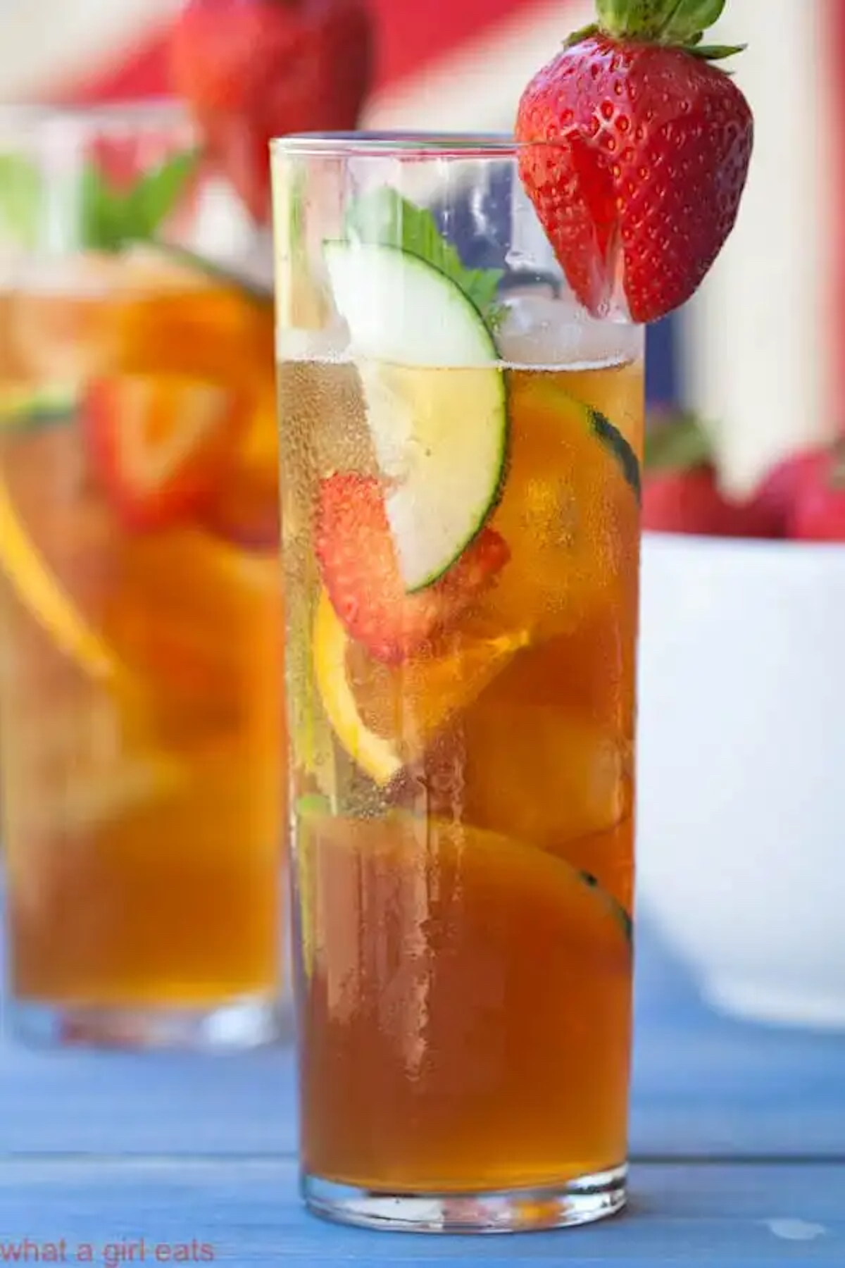 A tall glass filled with Pimm's Cup cocktail and fresh sliced fruit and veggies.