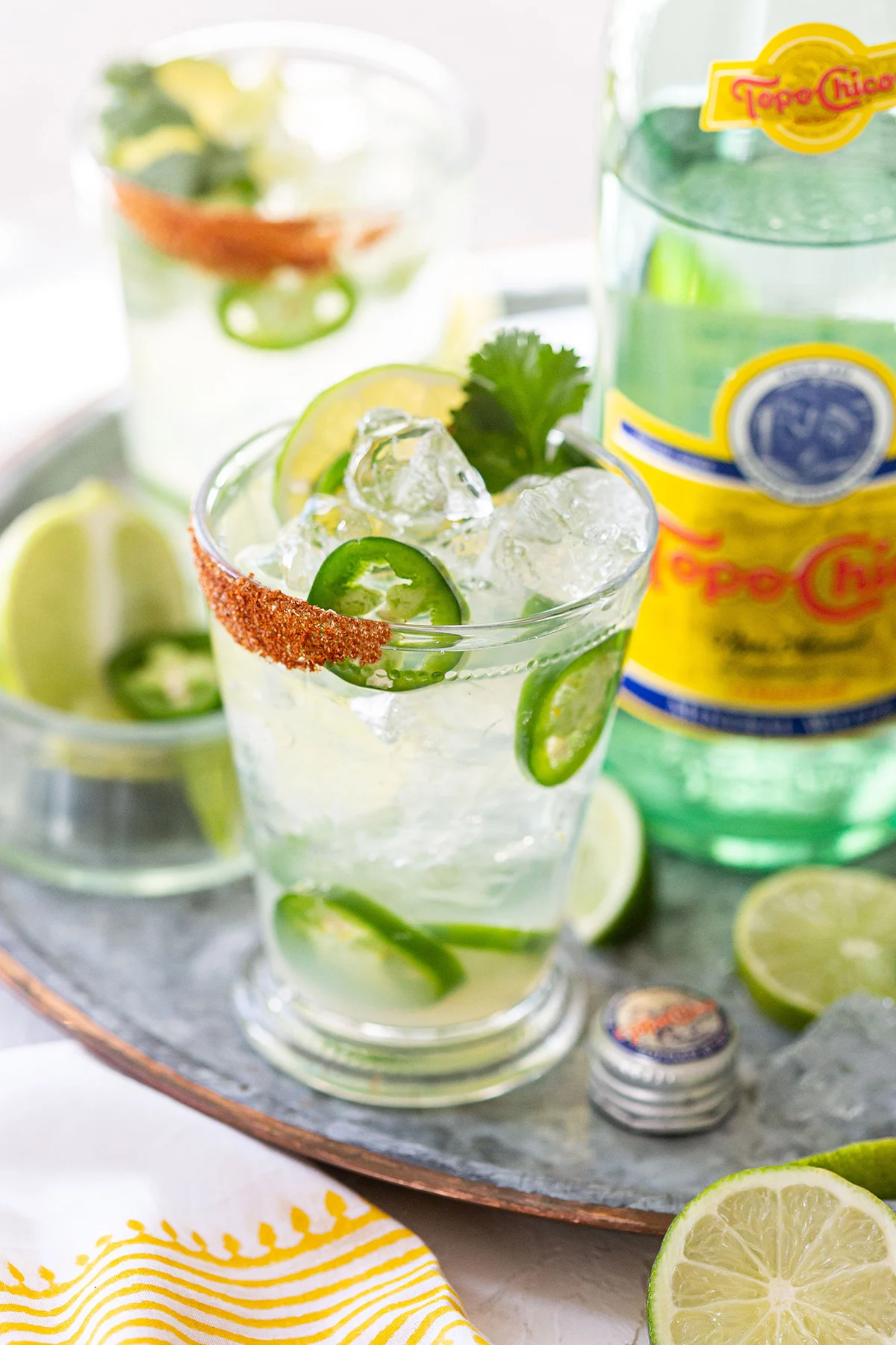 A pint glass filled with ranch water and jalapeno slices sits in front of a bottle of Topo Chico.