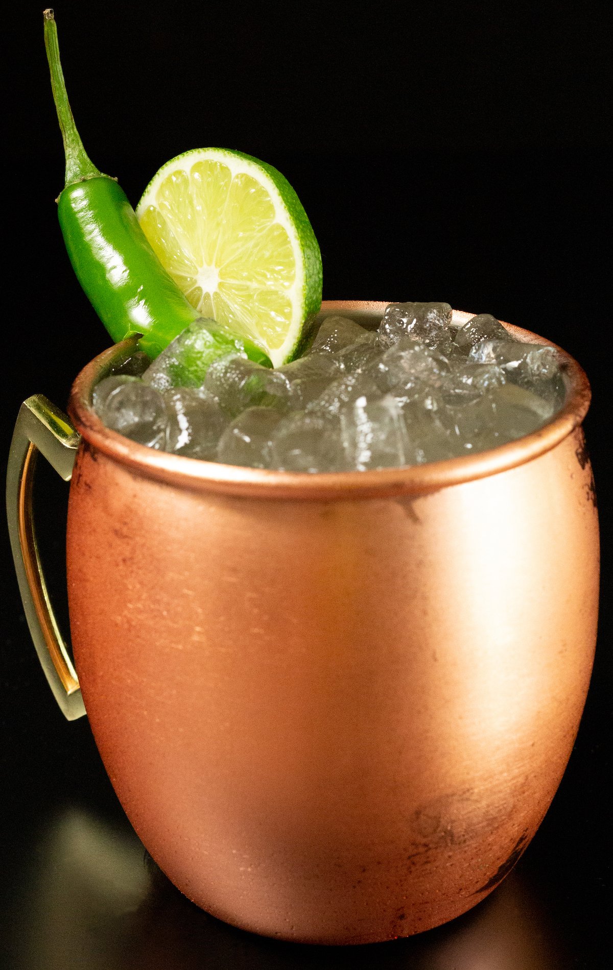 A copper moscow mule mug filled with a tequila Mexican mule sits on a black background.
