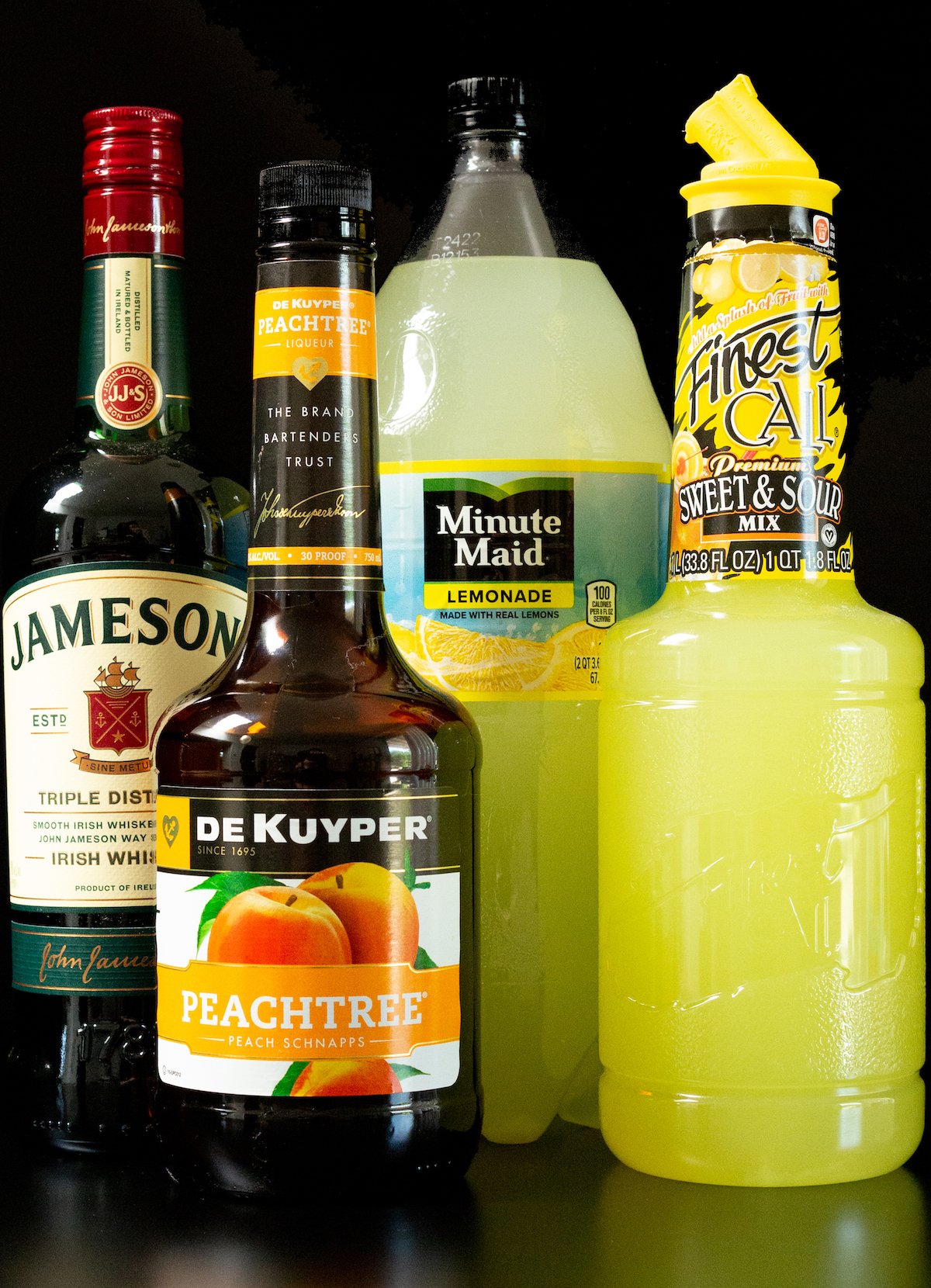 A bottle of Jameson, peach schnapps, lemonade, and sour mix on a black background.