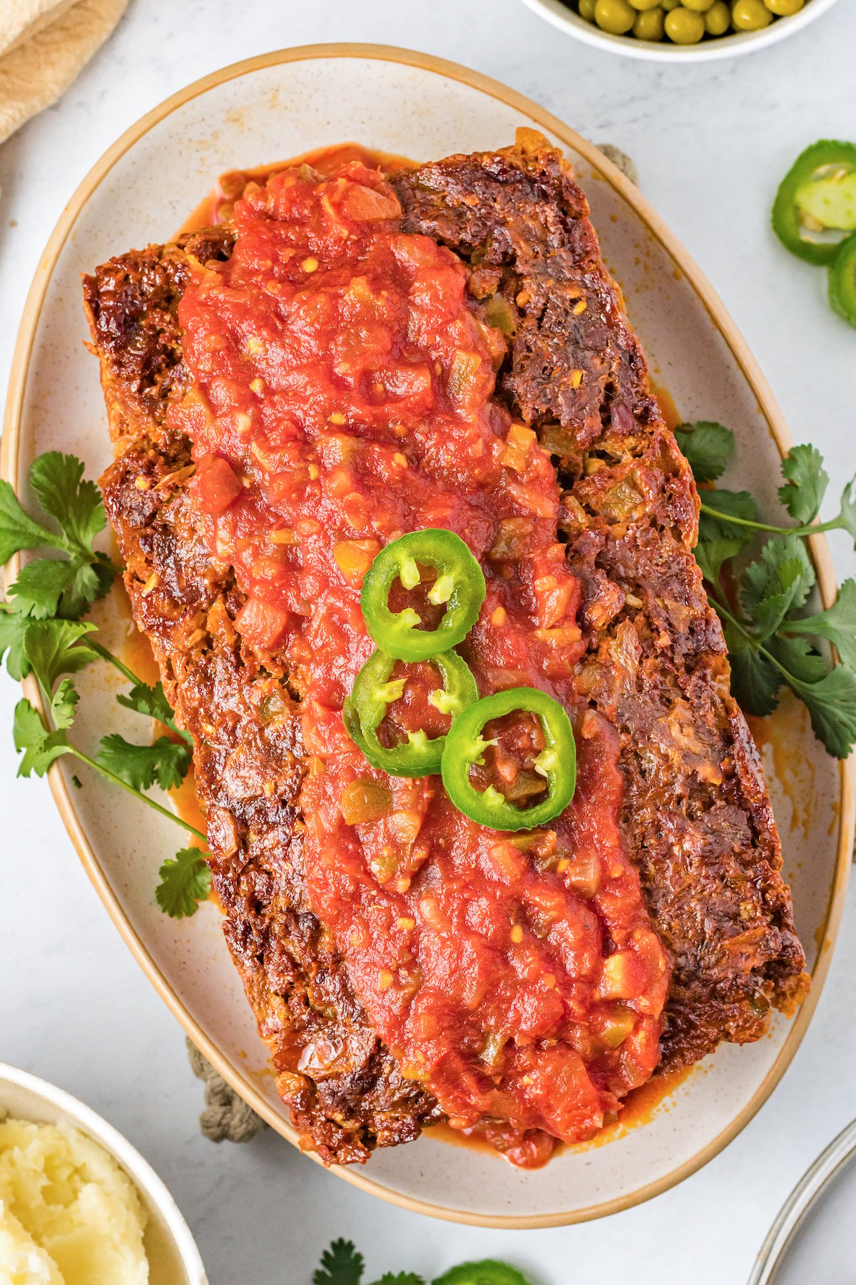 A Mexican meatloaf topped with salsa and sliced jalapeño on a serving platter.
