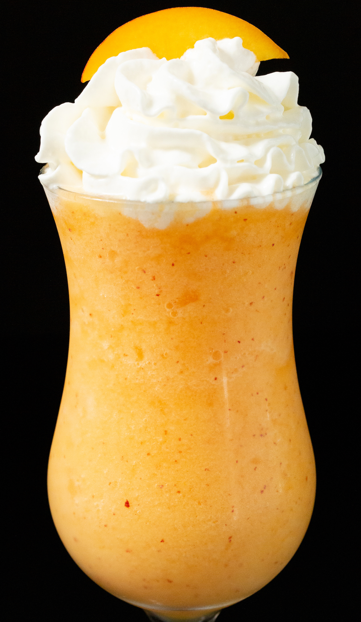 A hurricane glassed filled with a frozen peach daiquiri that's garnished with a peach slice and whipped cream.