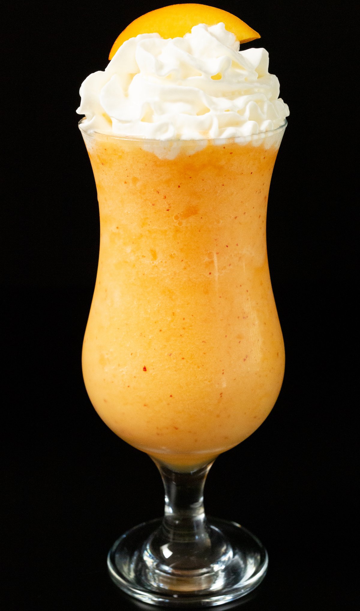 A hurricane glass filled with a peach frozen daiquiri with whipped cream on top. 