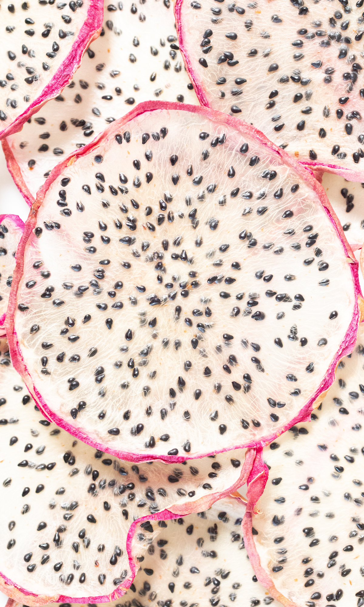 Close up of dehydrated slices of dragonfruit with pink peels and white flesh.