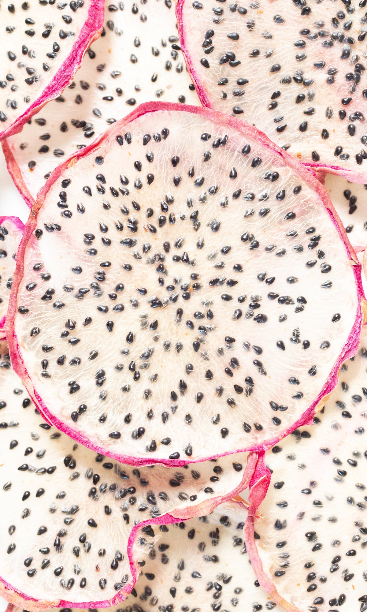 Close up of dehydrated slices of dragonfruit with pink peels and white flesh.