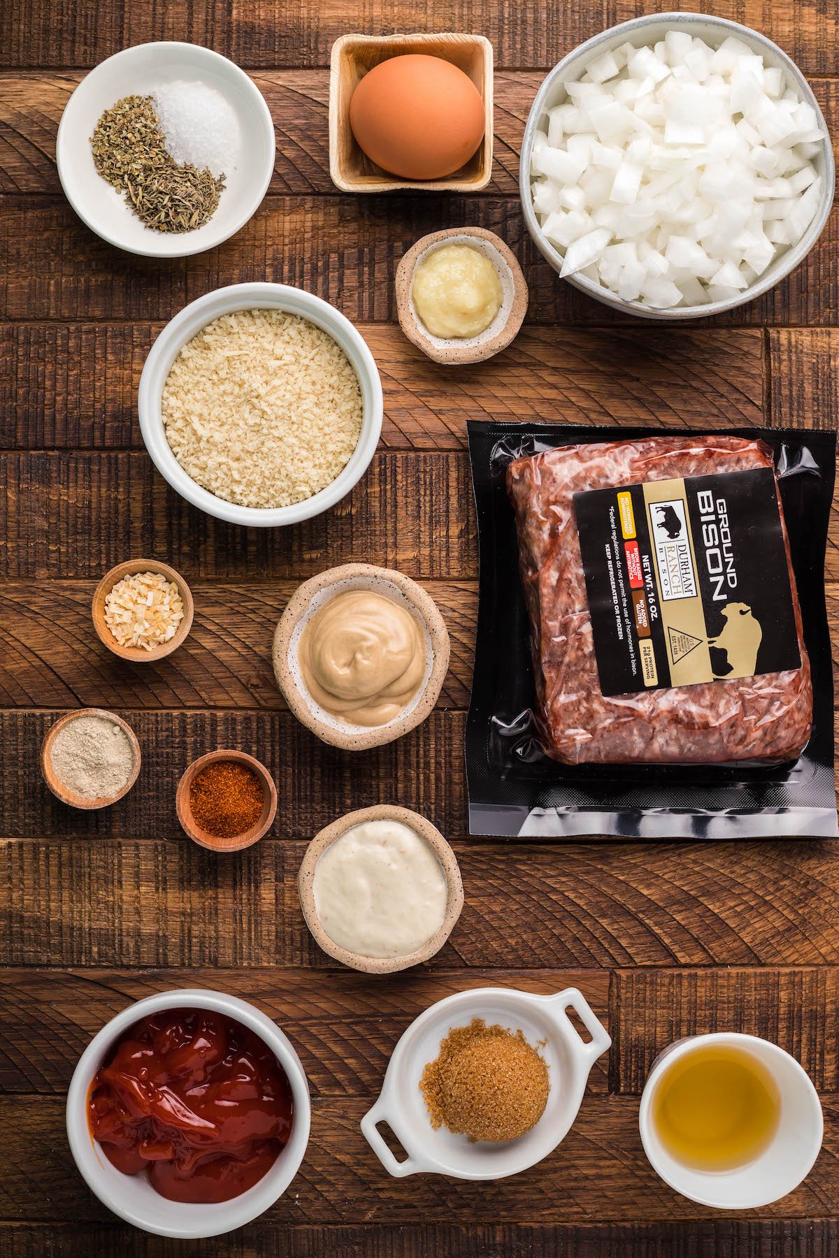 All the ingredients to make Bison meatballs in small prep bowls on a brown wood background.