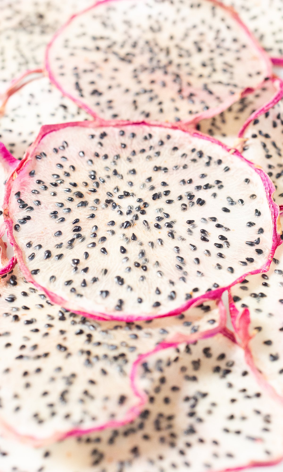 Dozens of slices of dehydrated dragon fruit on a white platter.