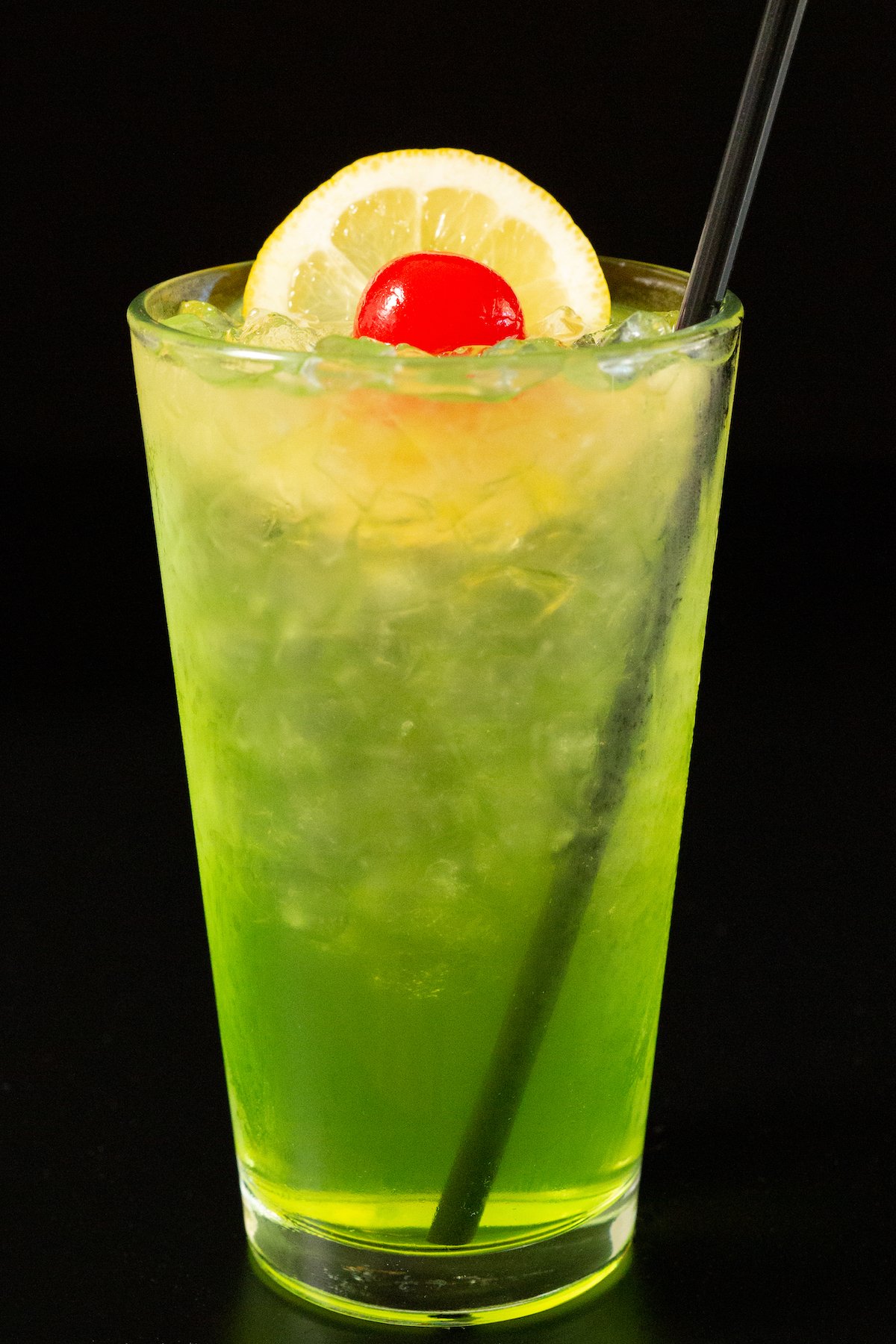 A neon green pint glass of Tokyo Iced Tea on a black background.