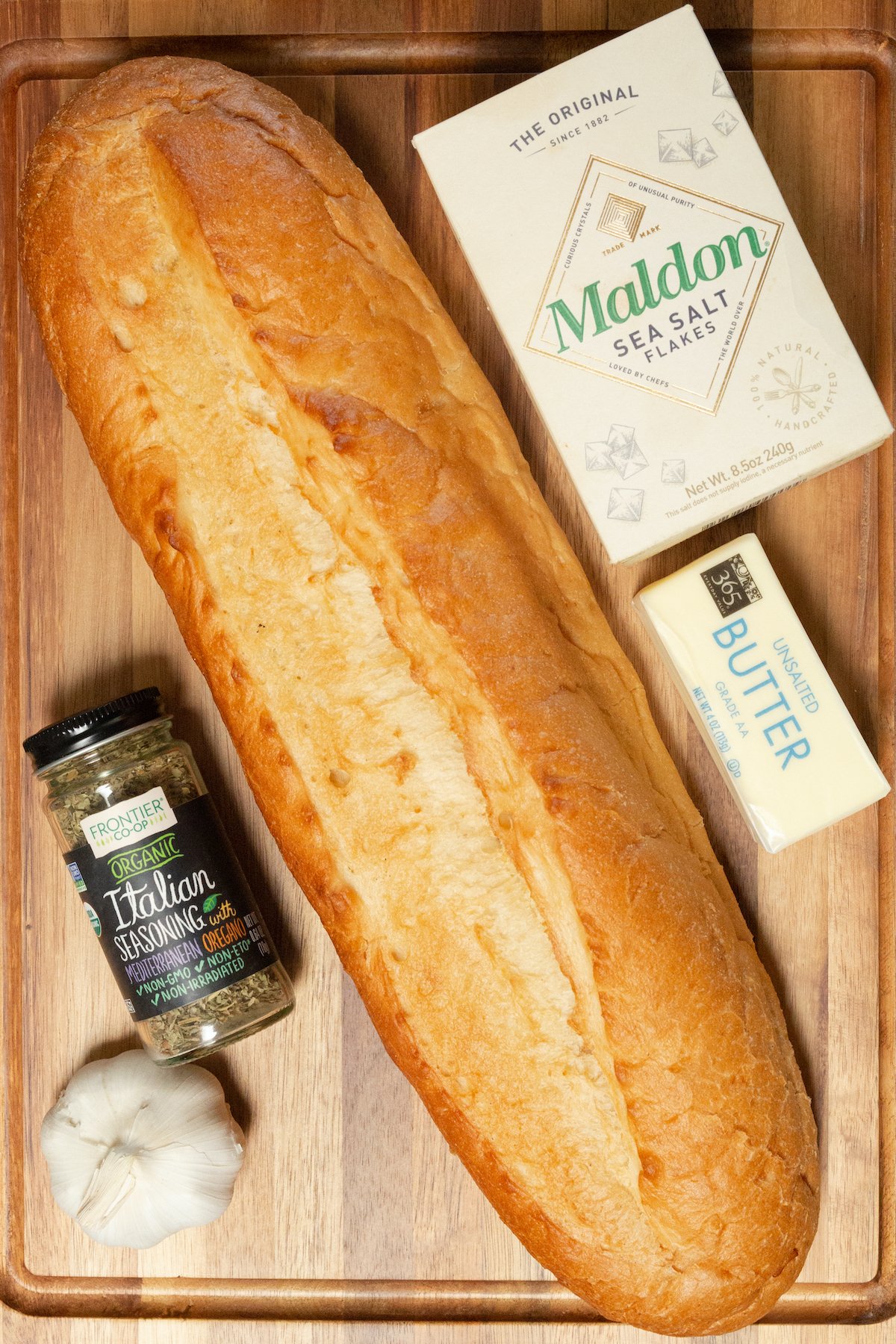 All the ingredients to make garlic bread in the air fryer arranged on a wood cutting board.