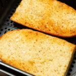 Two pieces of garlic bread french loaf in the air fryer basket.