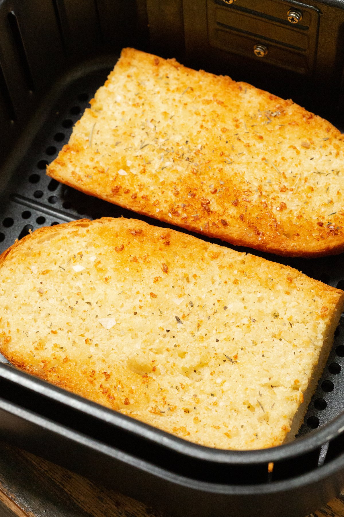 Two pieces of garlic bread french loaf in the air fryer basket.
