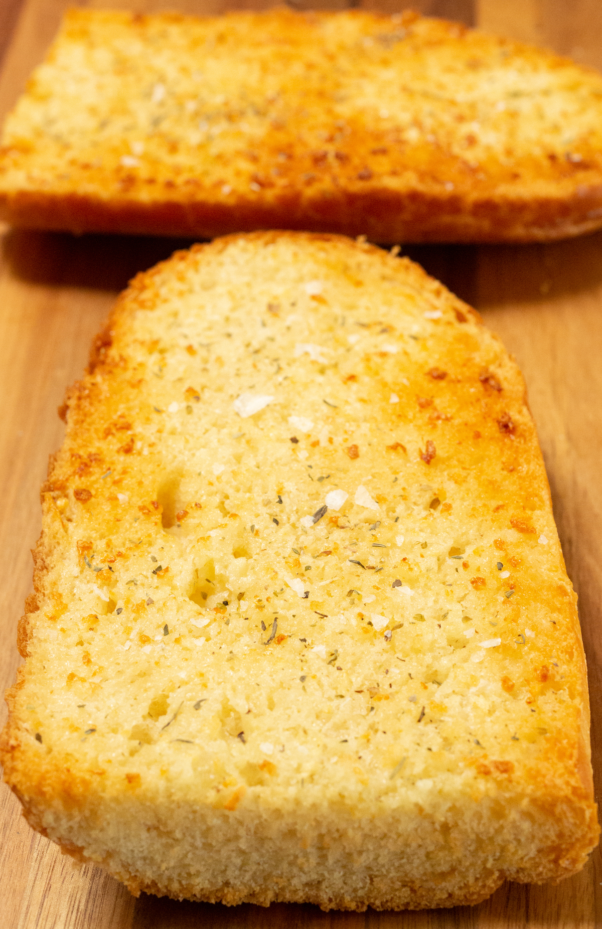 Two pieces of garlic bread made in the air fryer on a wood cutting board.
