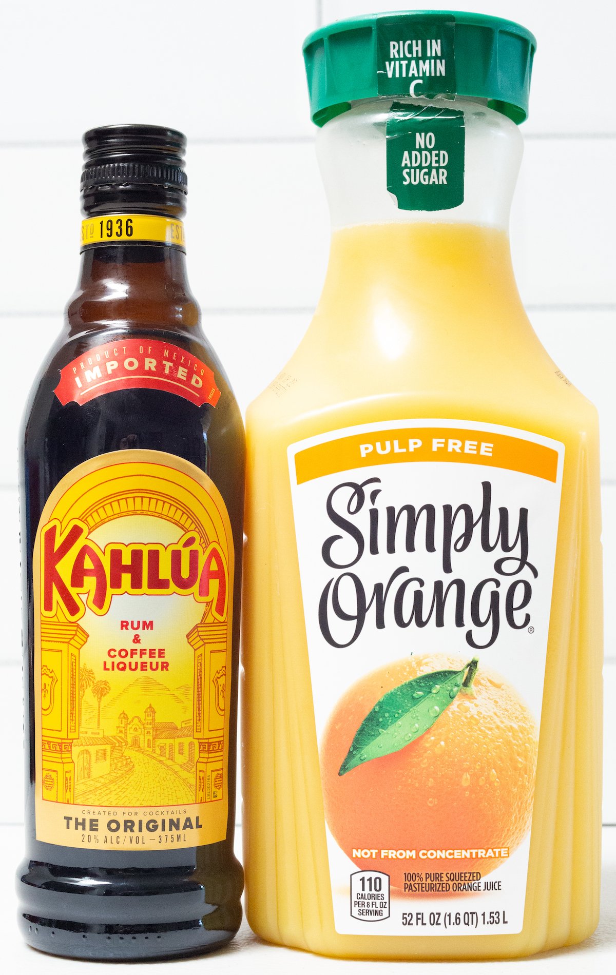 A bottle of Kahlua next to a bottle of orange juice in front of a white background.