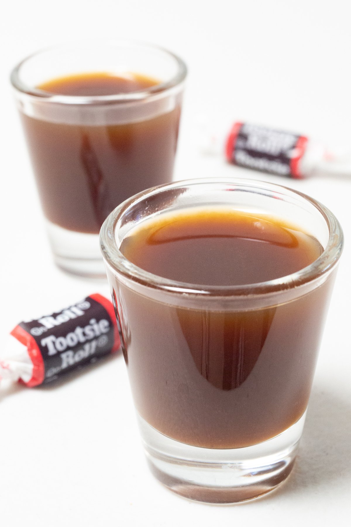 Two shot glasses filled with brown tootsie roll shots on a white background.