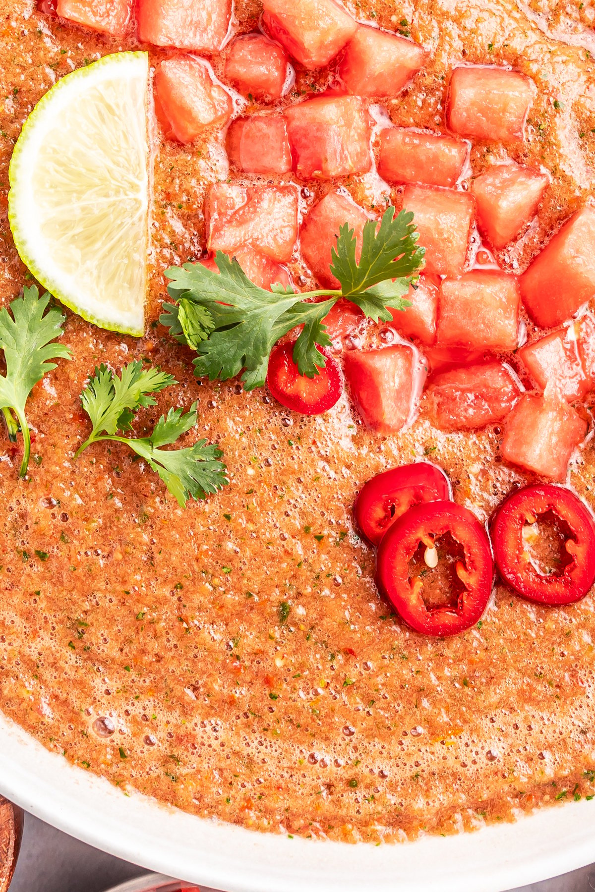 Close up of a while bowl filled with watermelon gazapcho that's topped with diced fruit, sliced peppers, and chopped herbs.