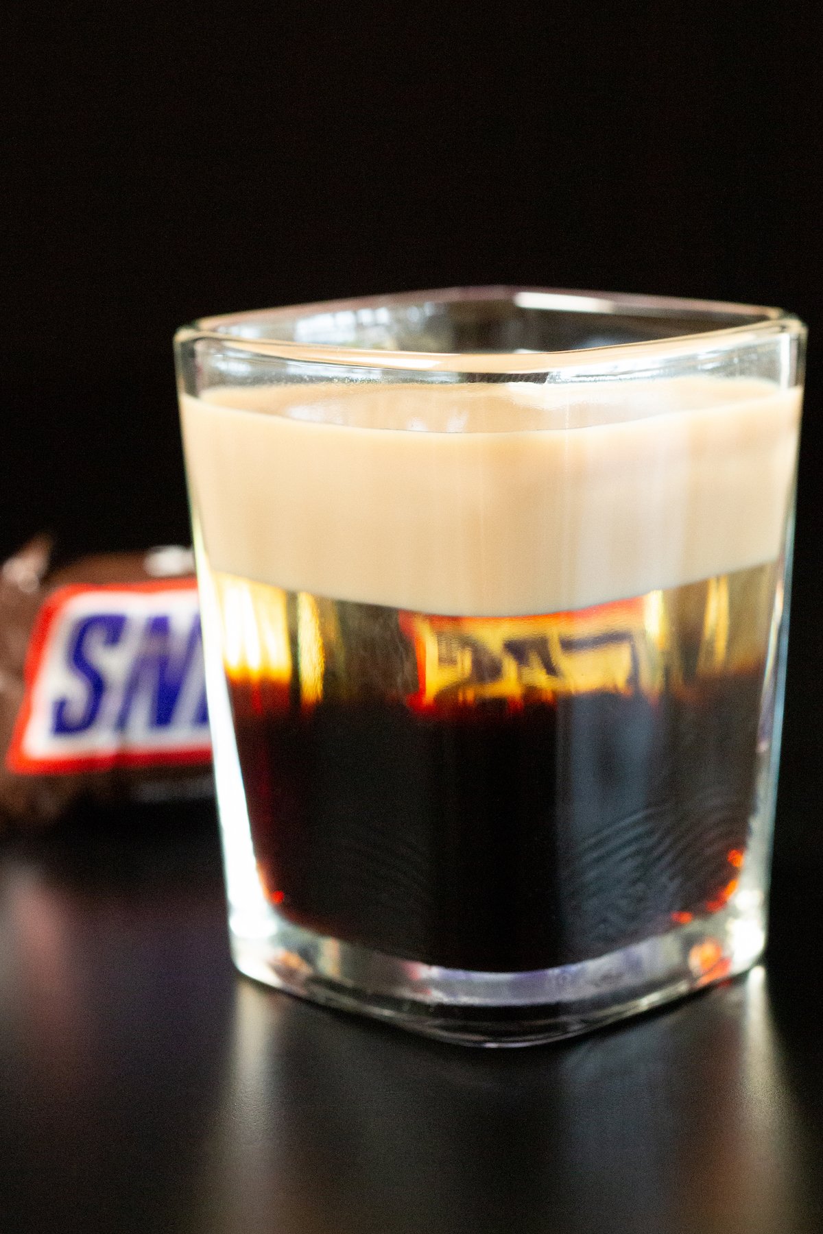 A square shot glass is filled with a snickers shot. You can see the three distinct liqueurs layered. 