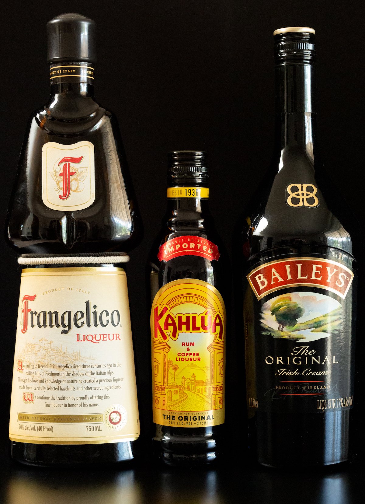 A bottle of Frangelico, Kahlua, and Bailey's Irish Cream on a black background.