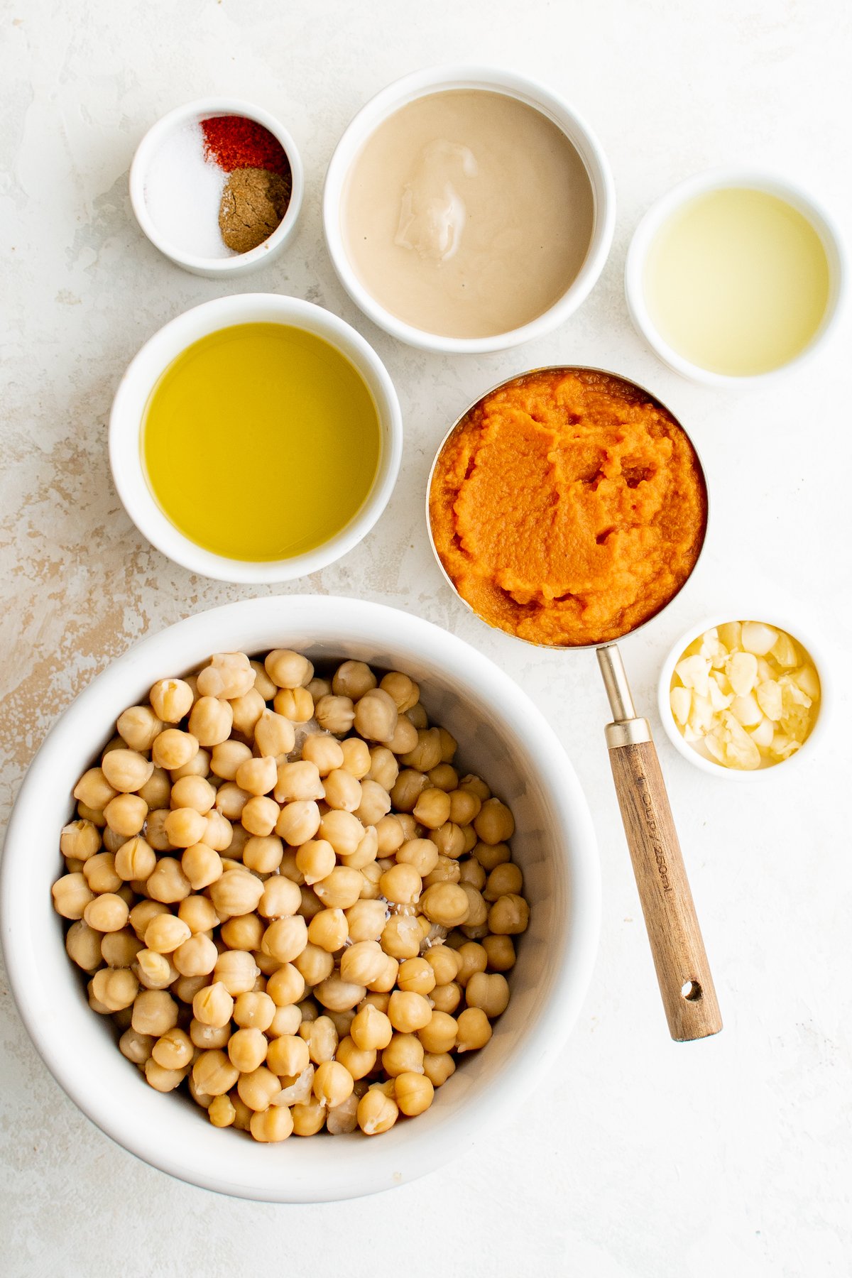 All of the ingredients to make pumpkin hummus in prep bowls and measuring cups.