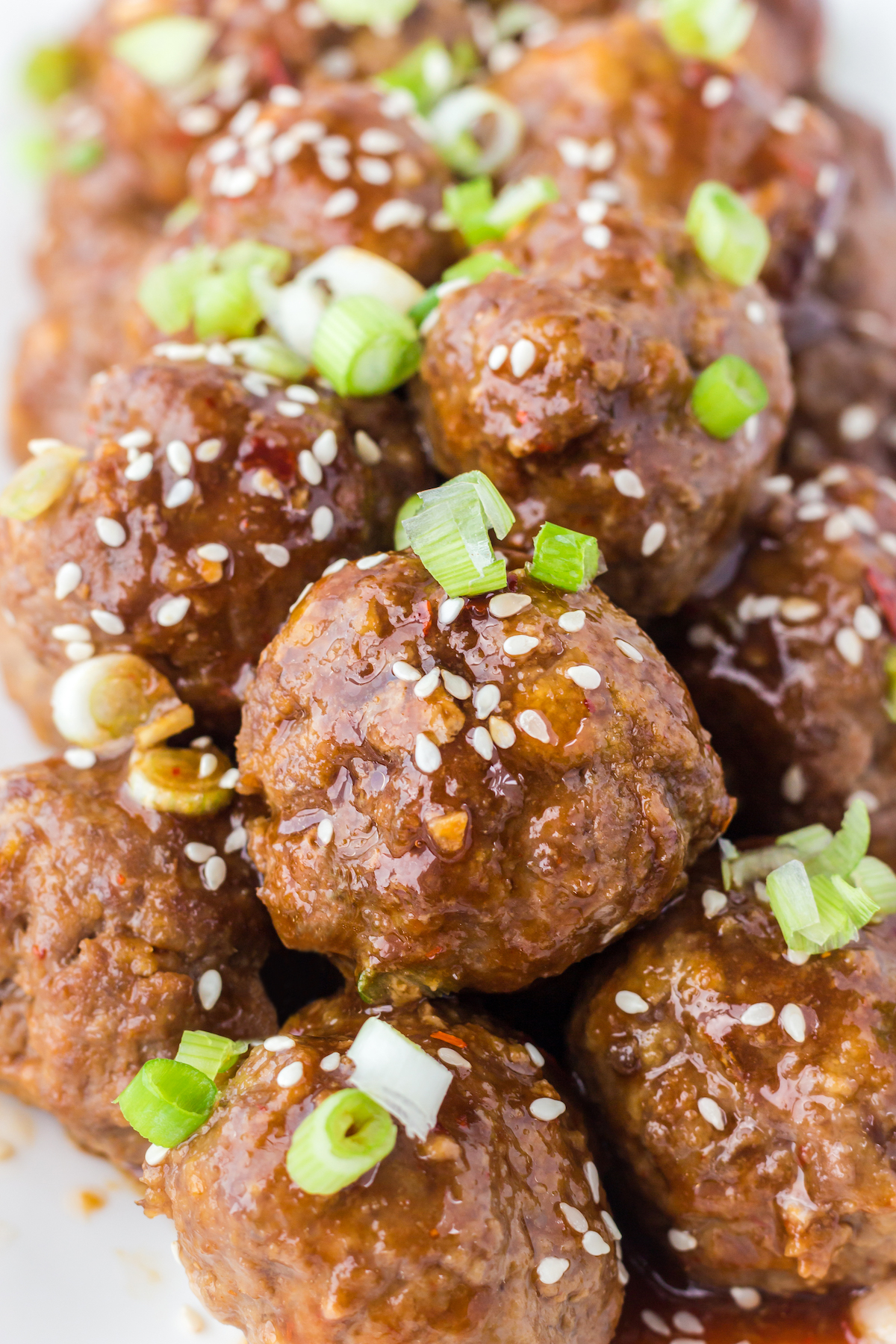 Dozens of asian meatballs covered in brown sauce, sesame seeds, and sliced green onions.