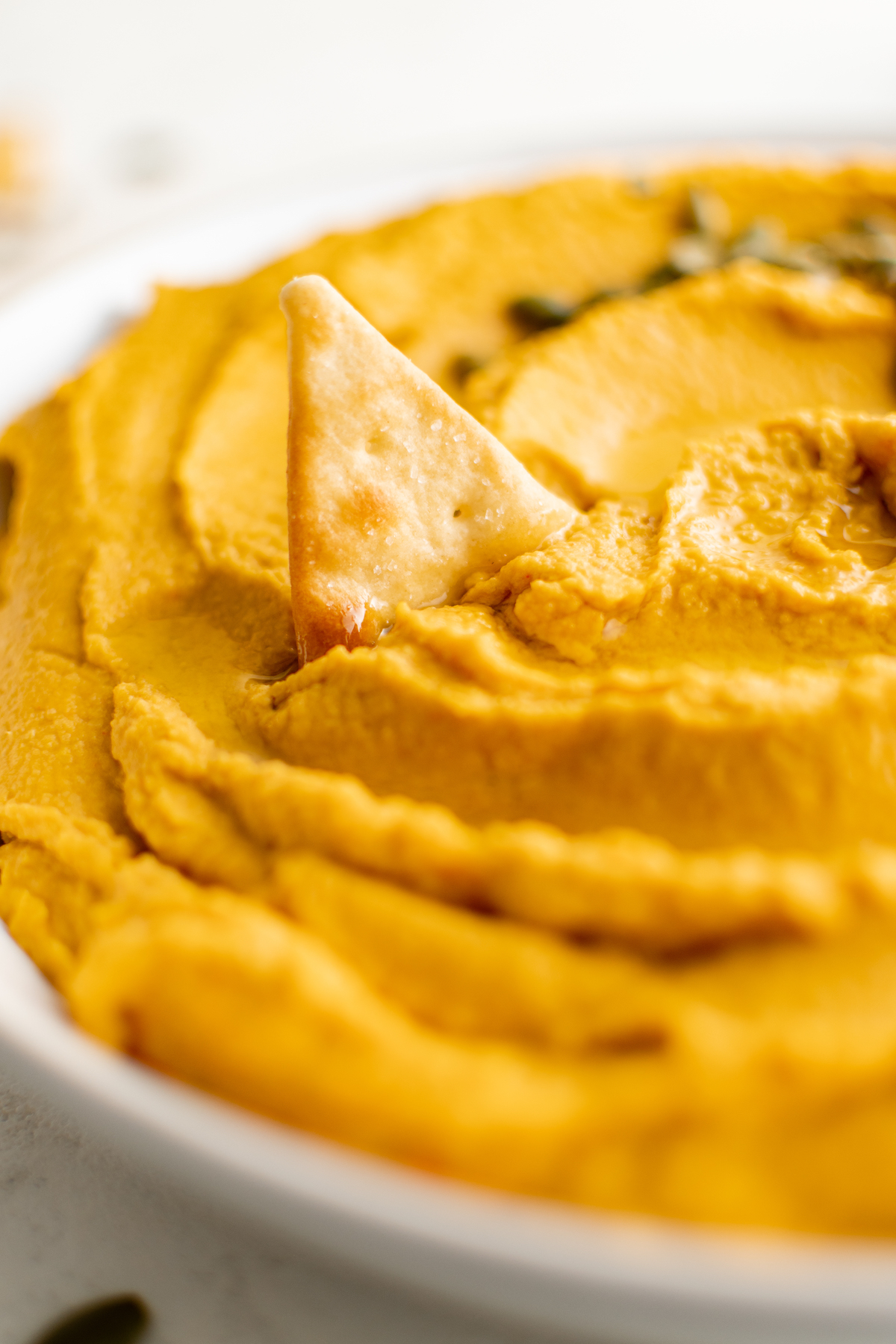 Close up of a bowl of orange pumpkin hummus with a pita chip half submerged.