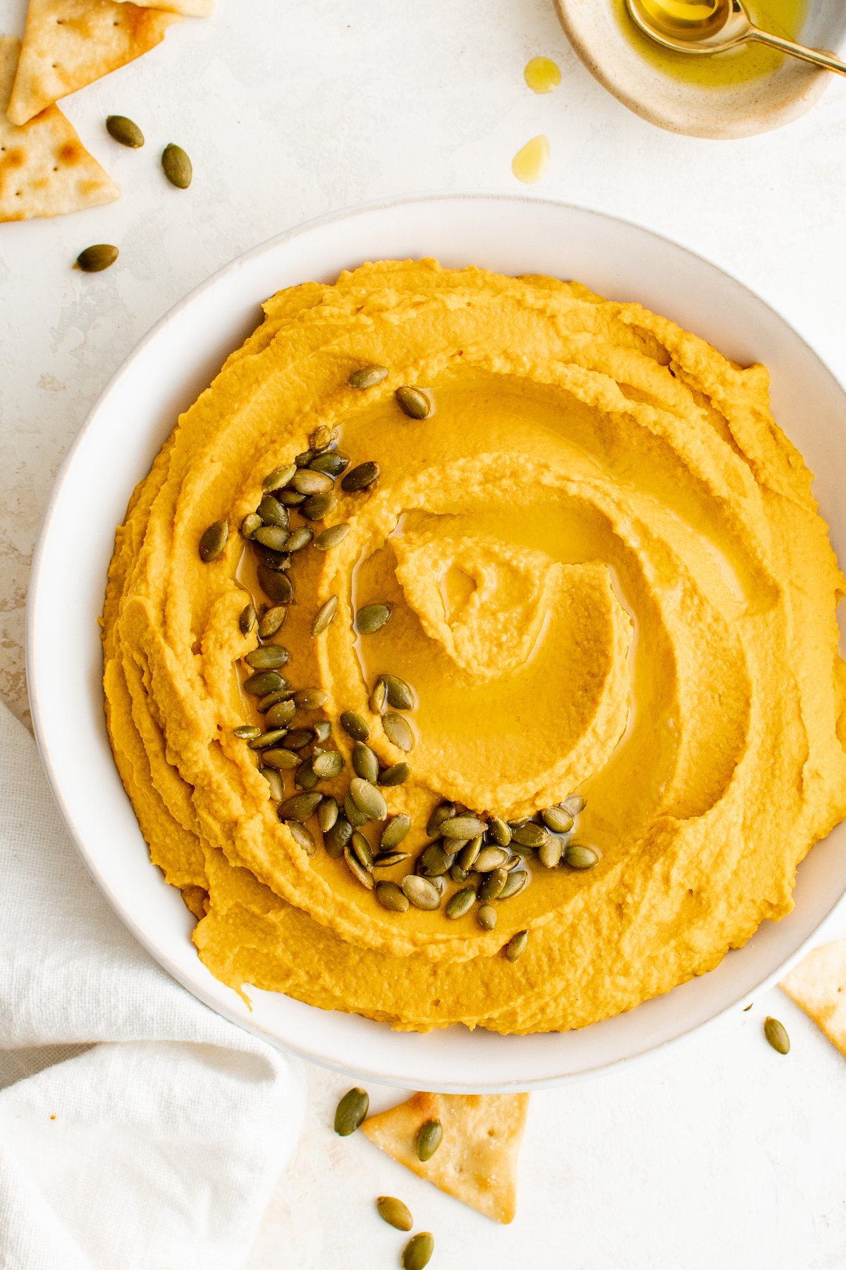 A white serving bowl filled with orange pumpkin hummus garnished with pepitas.