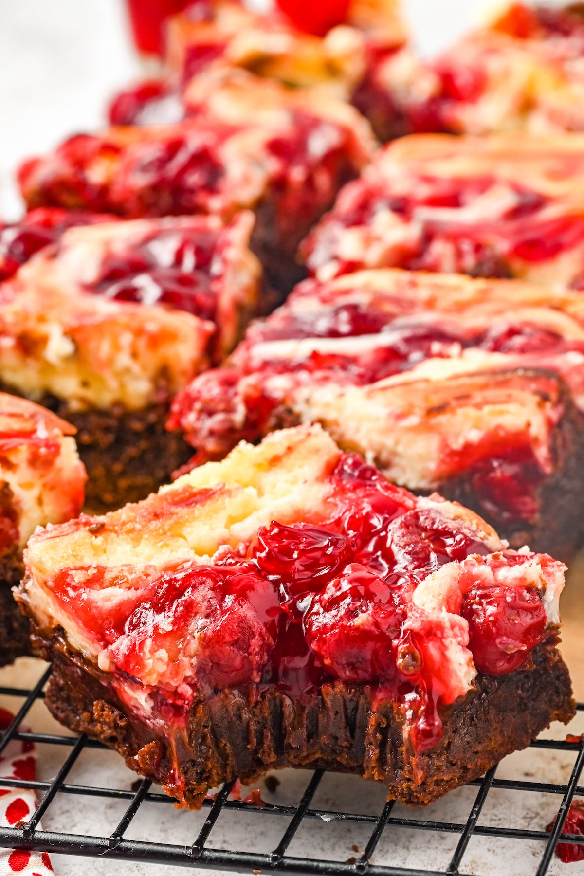 Cherry cheesecake brownie with a bite taken out of it. More brownies are out of focus in the background.