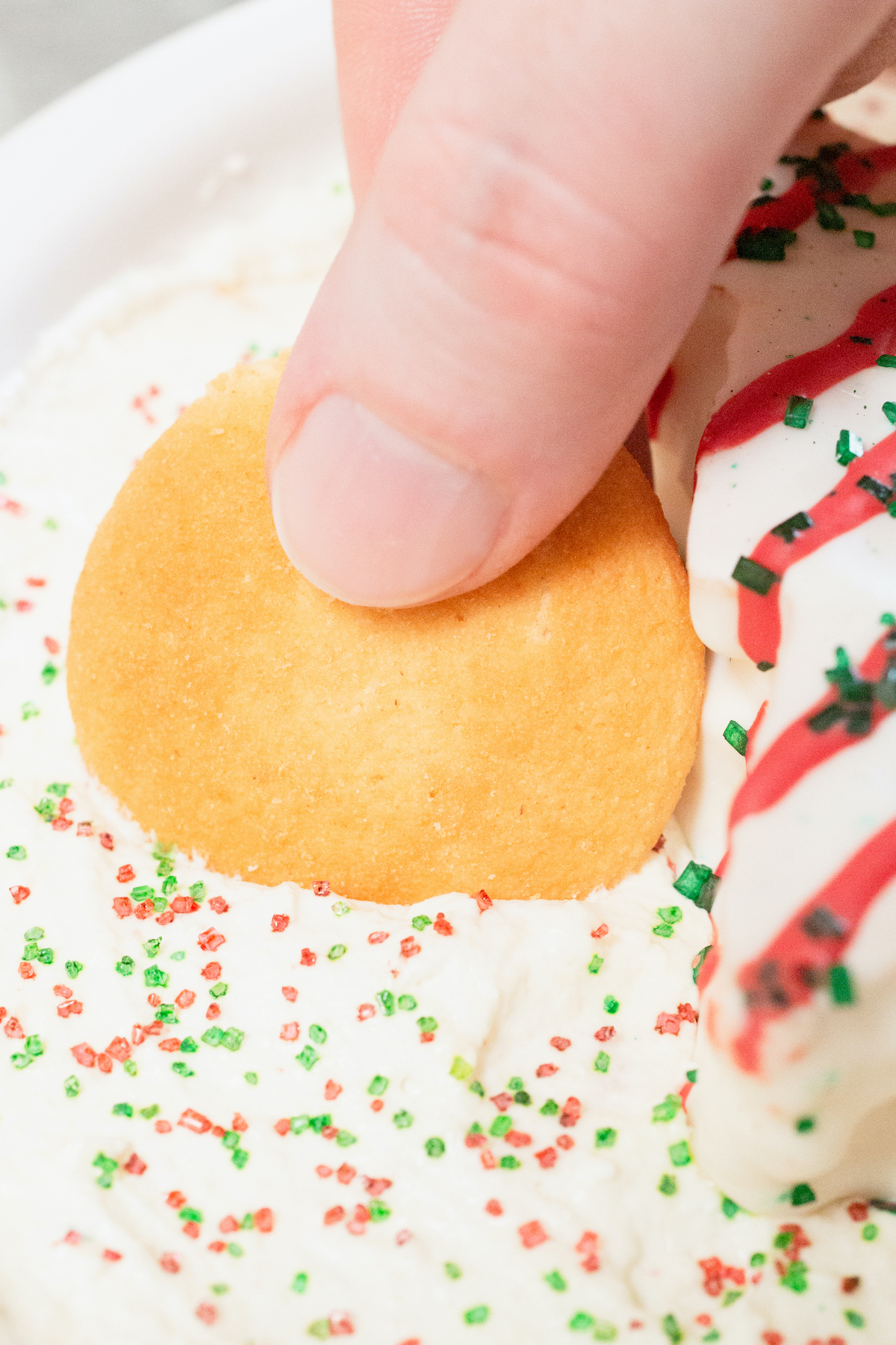 Close up of a finger dipping a Nilla wafer into Little Debbie's Christmas Tree Cake Dip.