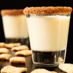 Two shot glasses each rimmed with cinnamon and sugar and filled with a Cinnamon Toast Crunch shot. Pieces of the cereal surround them.