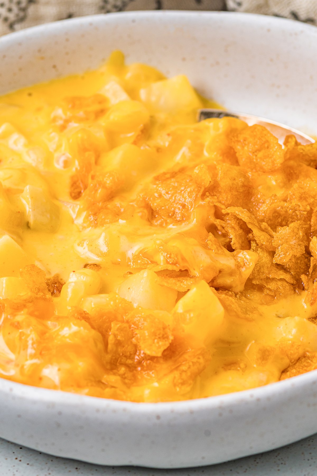 Close up of a serving of cheesy hash brown casserole in a white bowl.