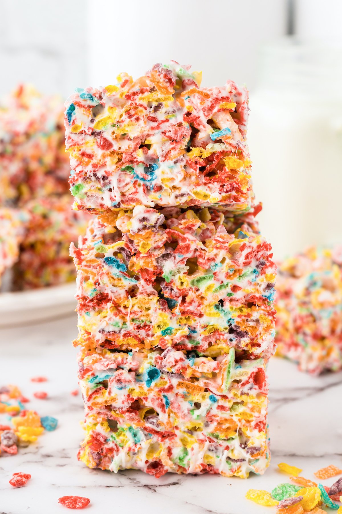 Three colorful fruity pebbles treat squares stacked on top on one another in front of a white background.