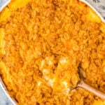 Overhead view of white oval baking dish filled with orange, cheesy funeral potatoes topped with cornflakes.