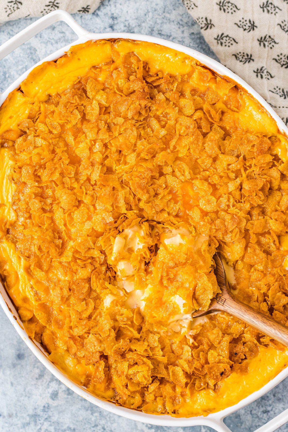 Overhead view of white oval baking dish filled with orange, cheesy funeral potatoes topped with cornflakes.