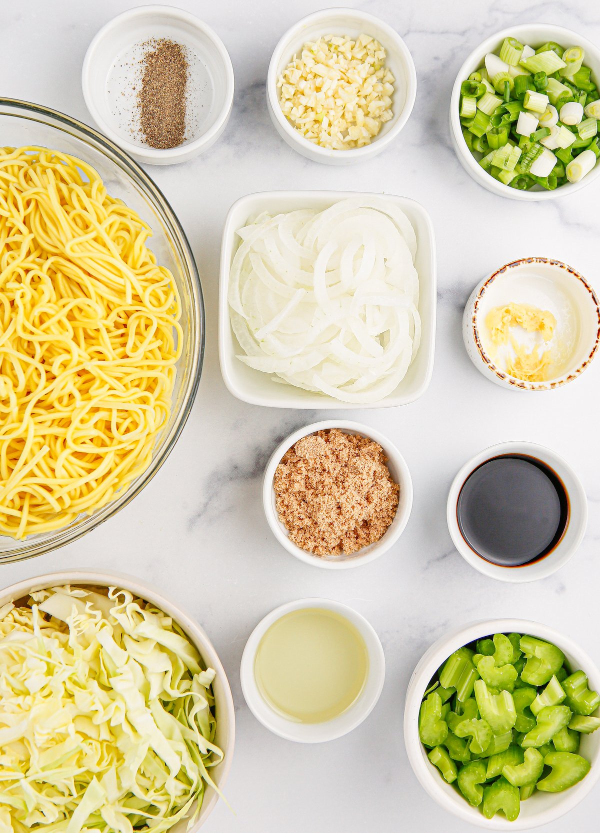 All the ingredients to make Panda Express chow mein in prep bowls on a white marble background.