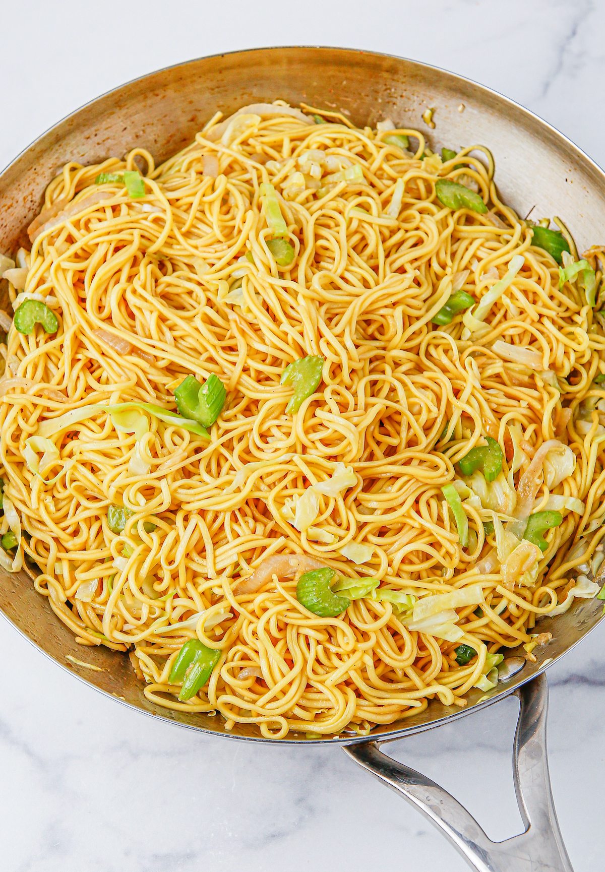 A sautee pan filled with cooked chow mein noodles garnished with sliced green onion.