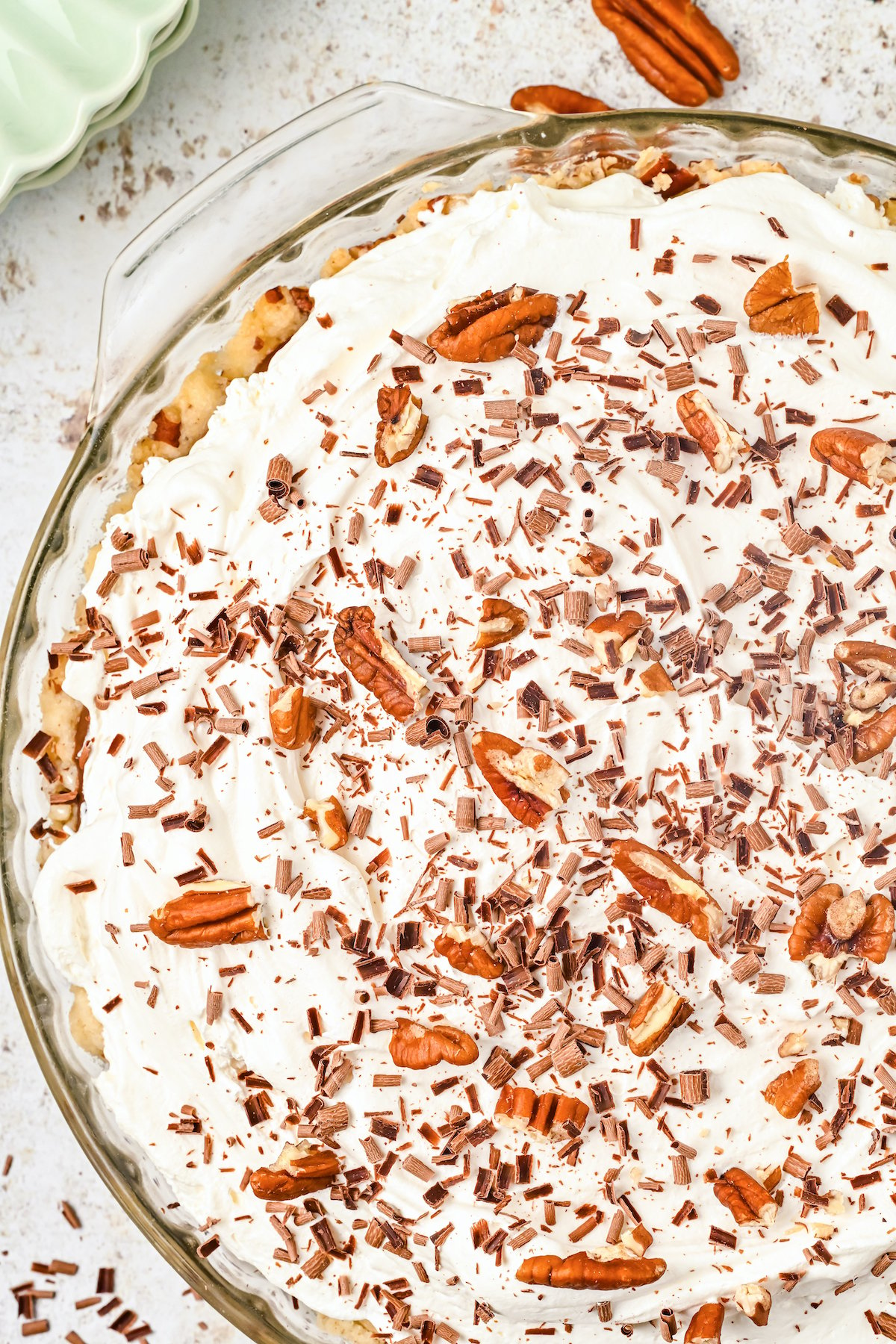 A glass pie dish filled with a possom pie that's topped with cool whip and roughly chopped pecans.