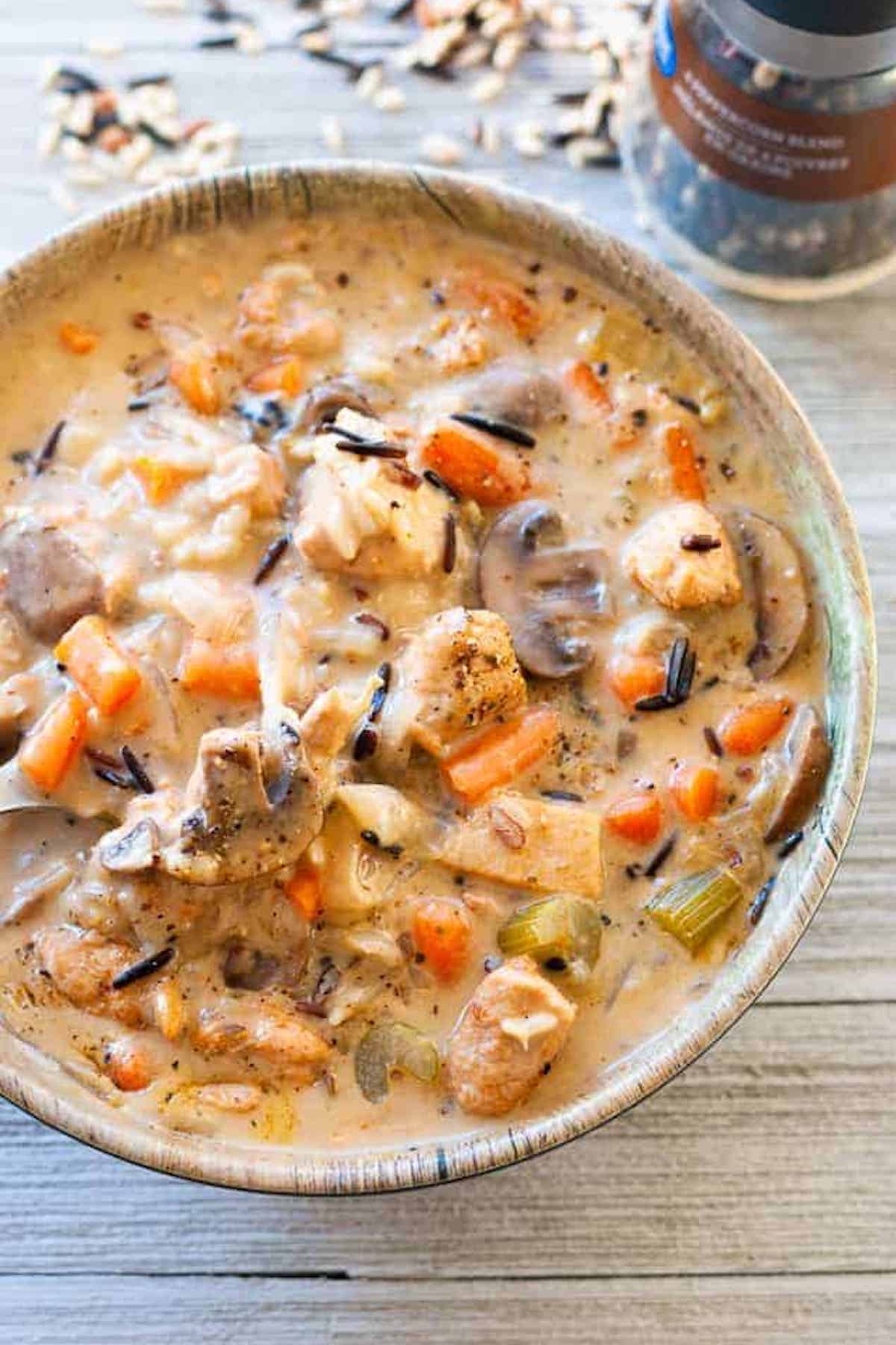 A bowl filled with cream chicken and wild rice soup with sliced mushrooms, celery, and carrots.