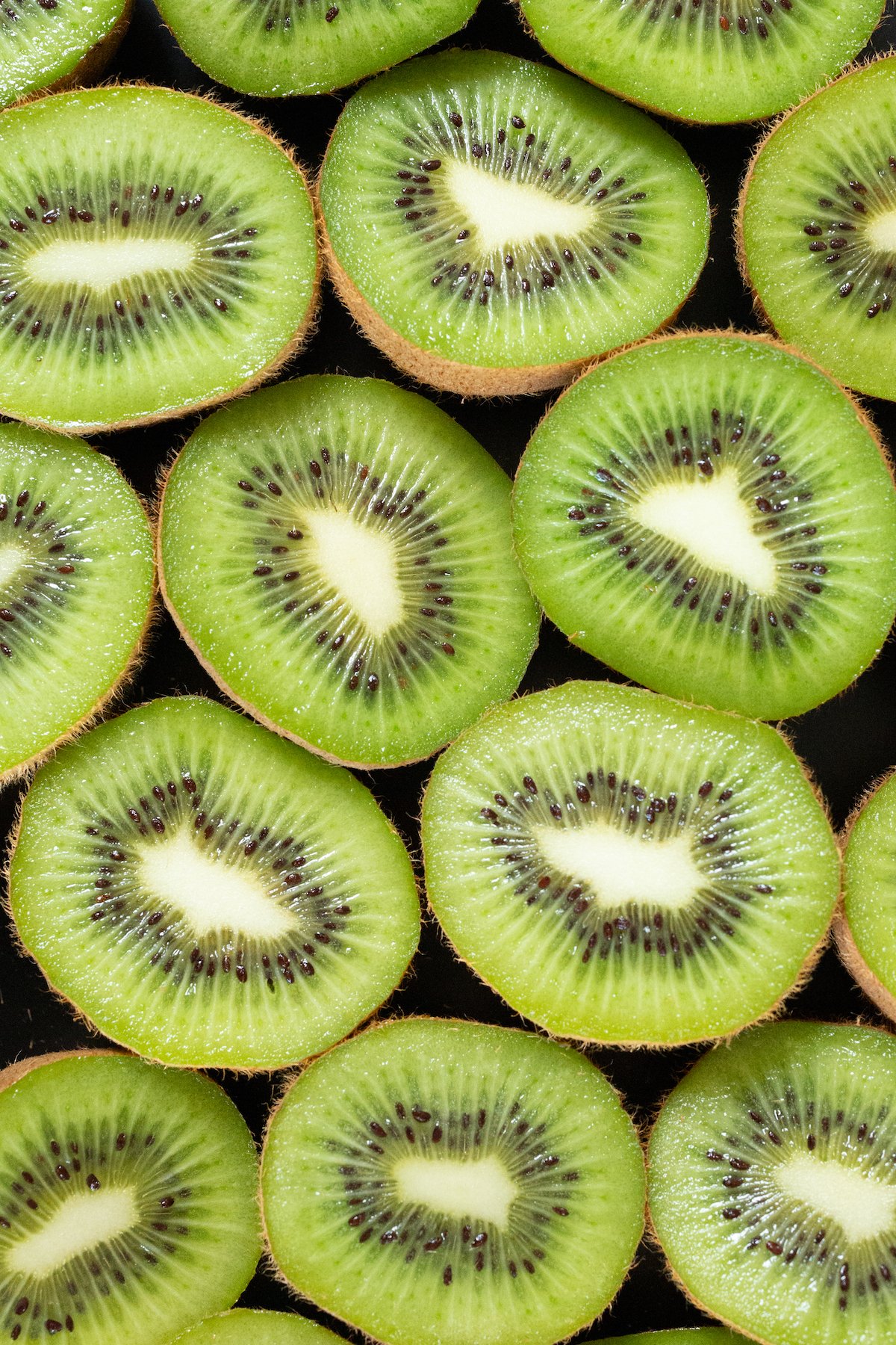 Overhead look at about a dozen of green kiwis that have been sliced in half.