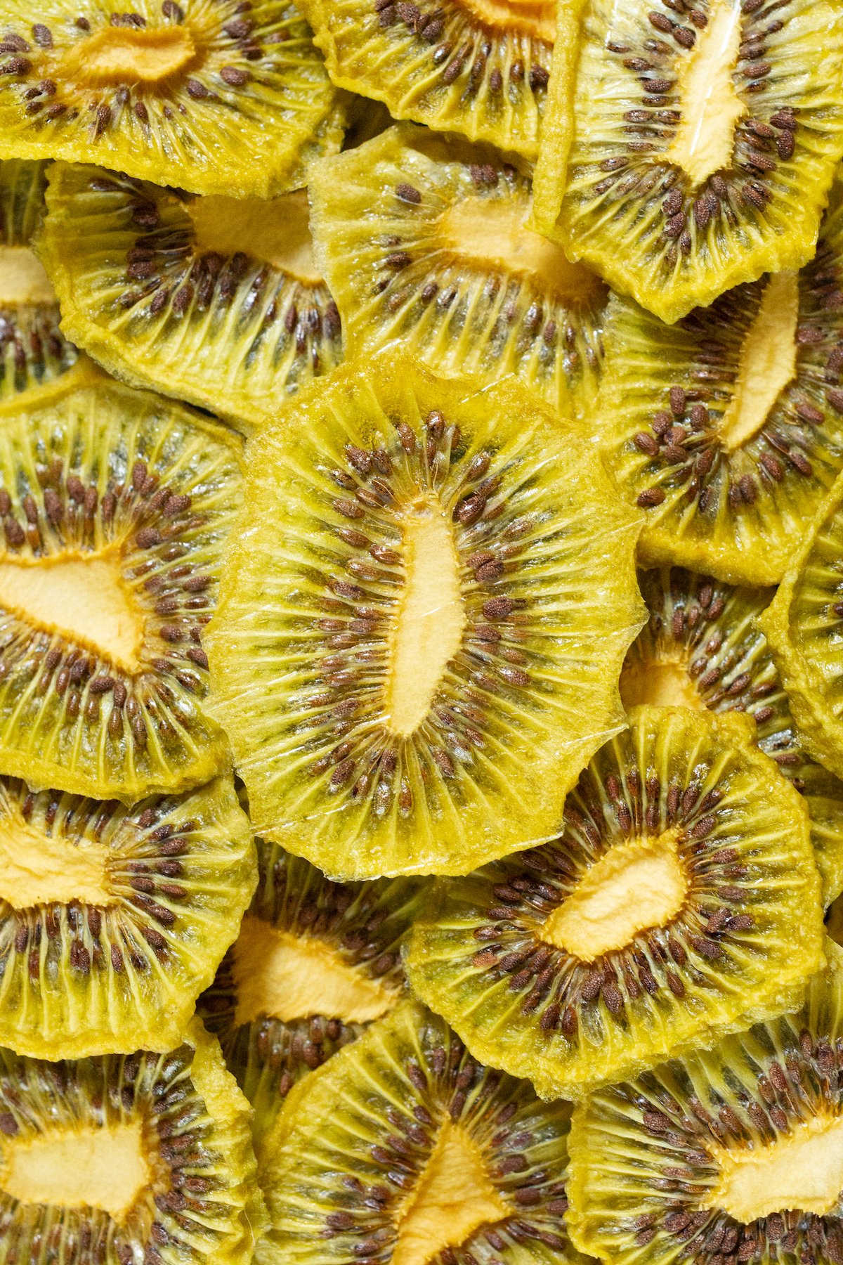 Close up of dozens of dehdyrated kiwi chips stacked on top of and around each other.