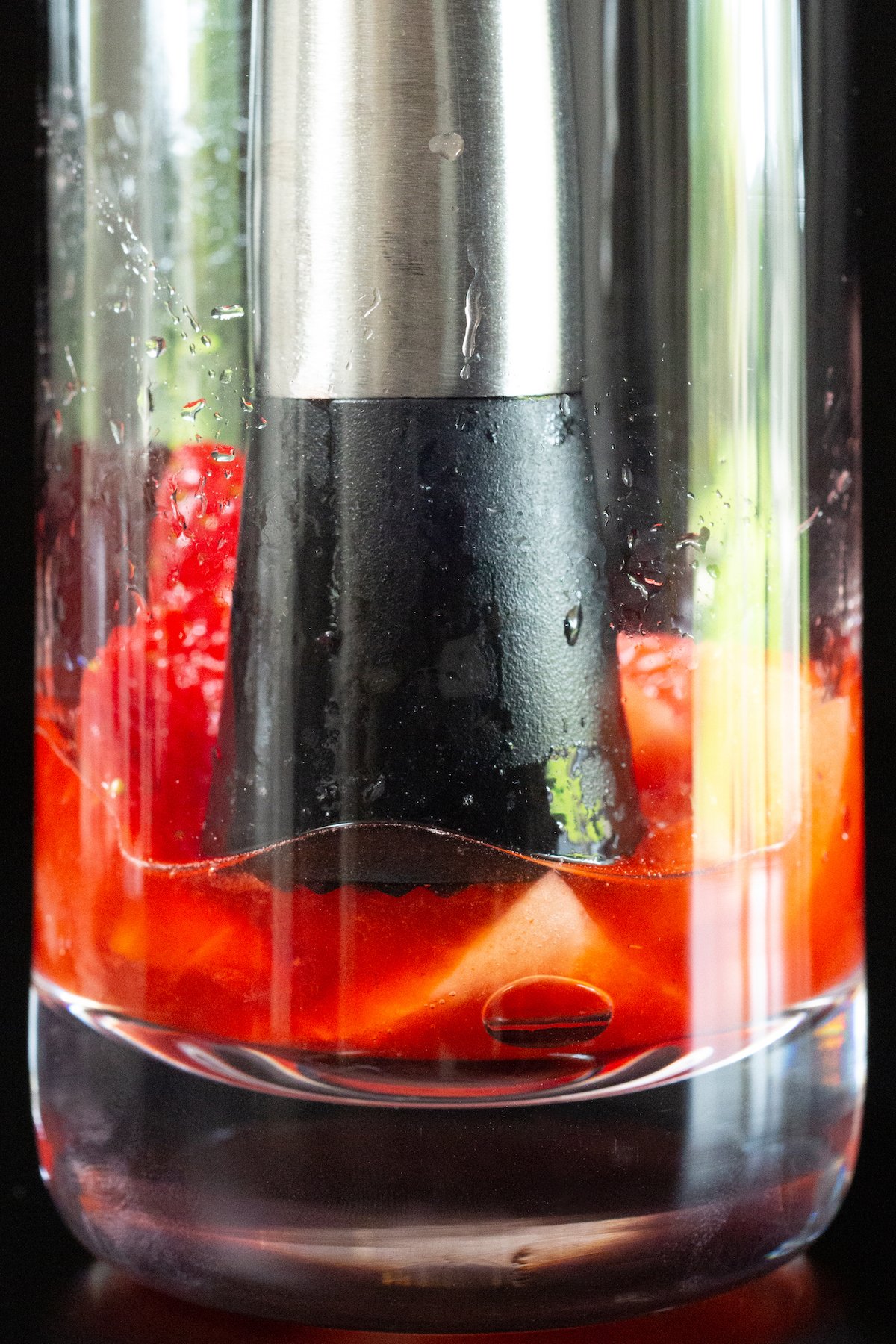 Close up of a highball glass with slice strawberries in the bottom being muddled.