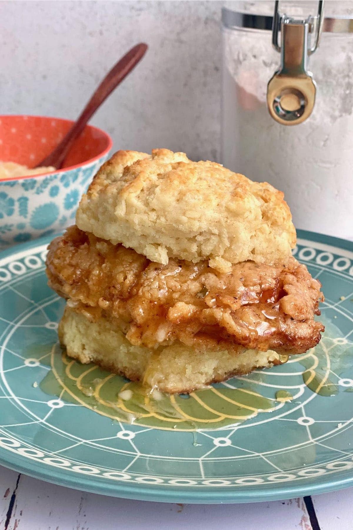A fried chicken fillet covered in honey on a buttermilk biscuit.