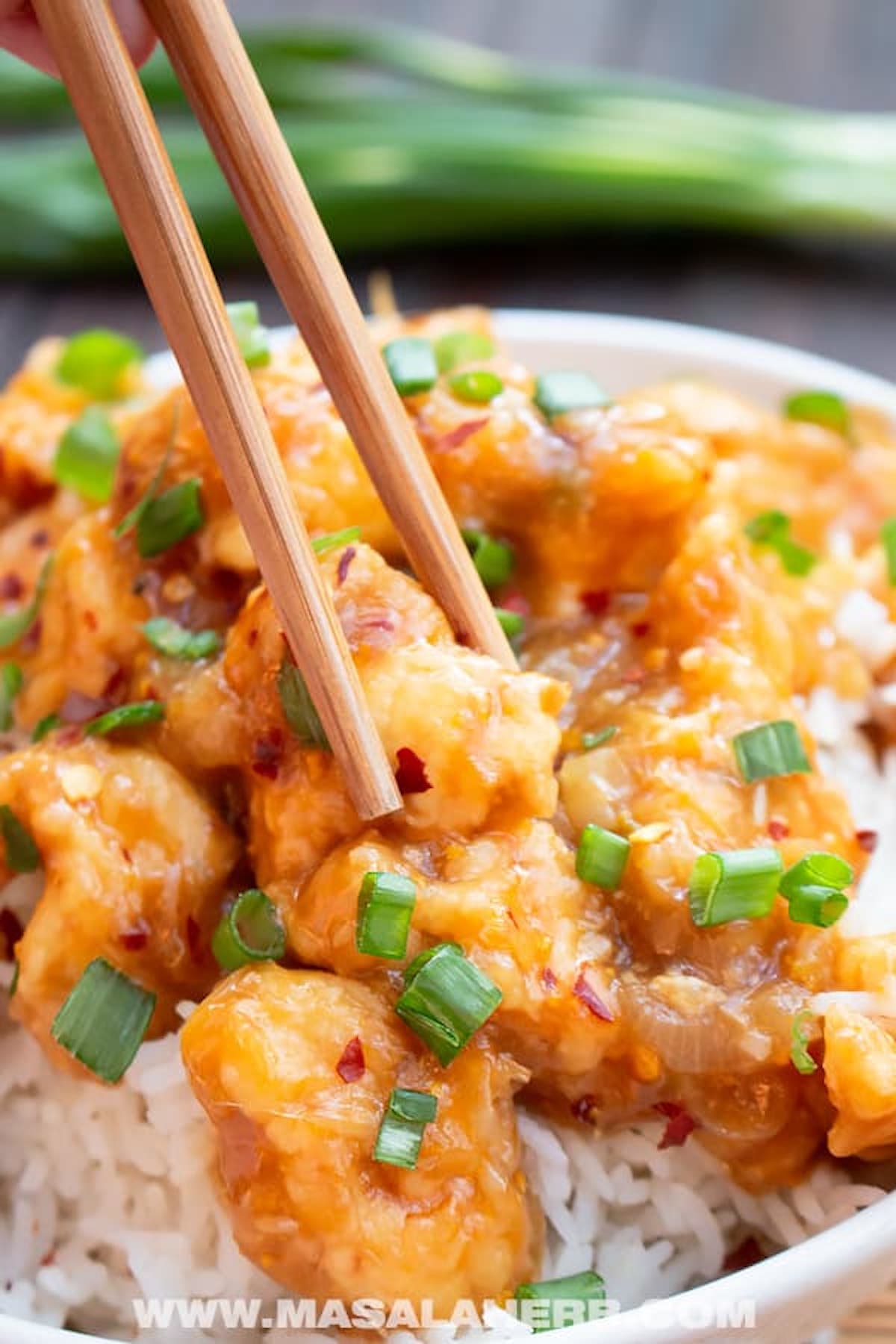 A white bowl filled with white rice that's topped with copycat Panda Express orange glazed chicken nuggets.