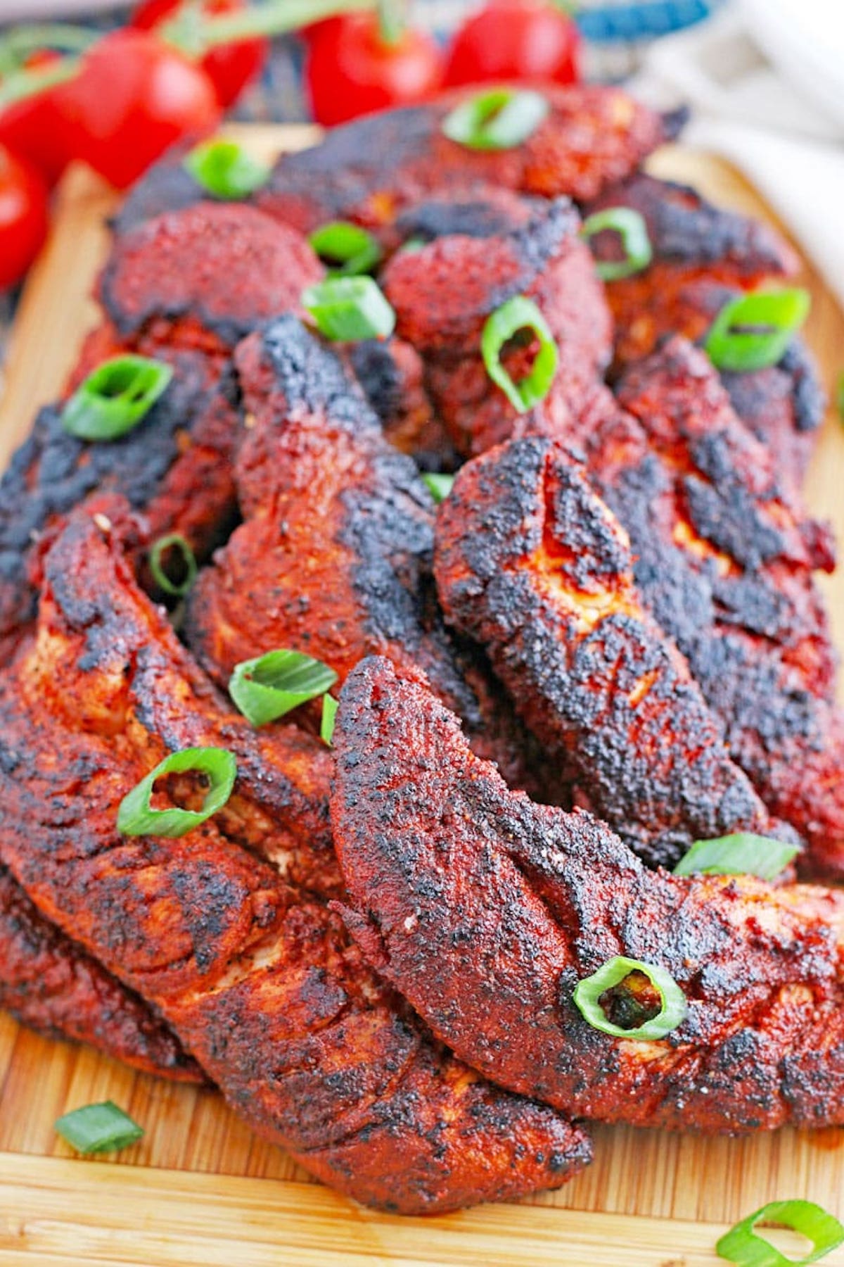 A cutting board filled with about a dozen copycat Popeyes blackened chicken strips garnished with green onion slices.