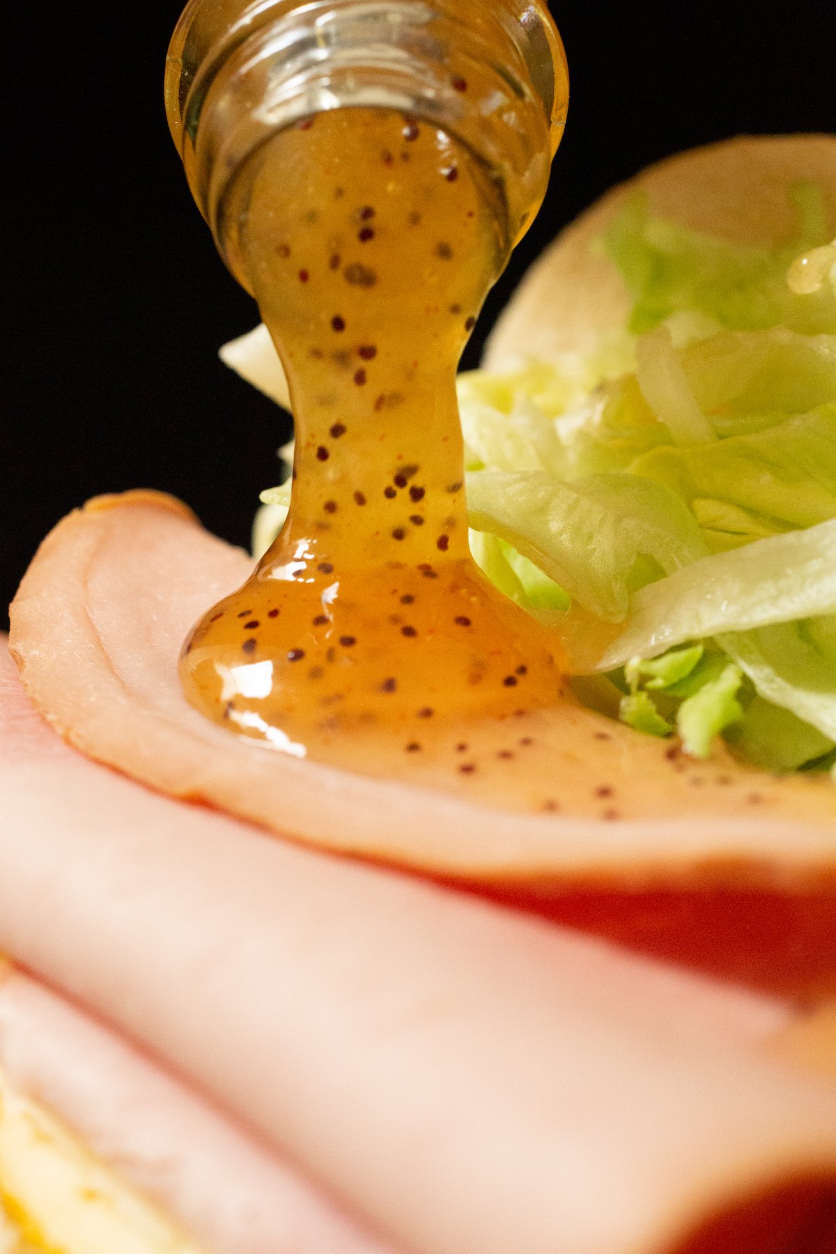 Copycat sweet onion sauce being poured out of the bottle onto a ham sandwich.