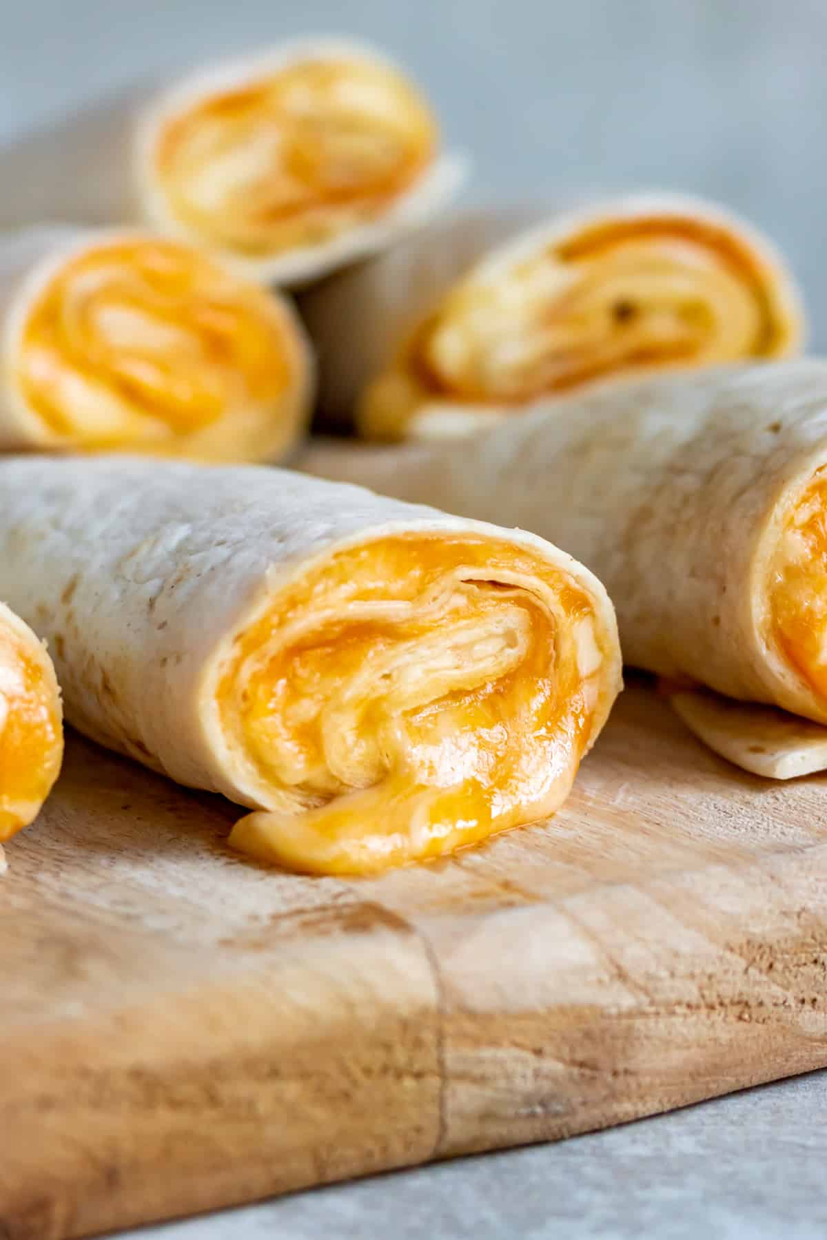 Several tortilla roll ups oozing cheese on a cutting board.