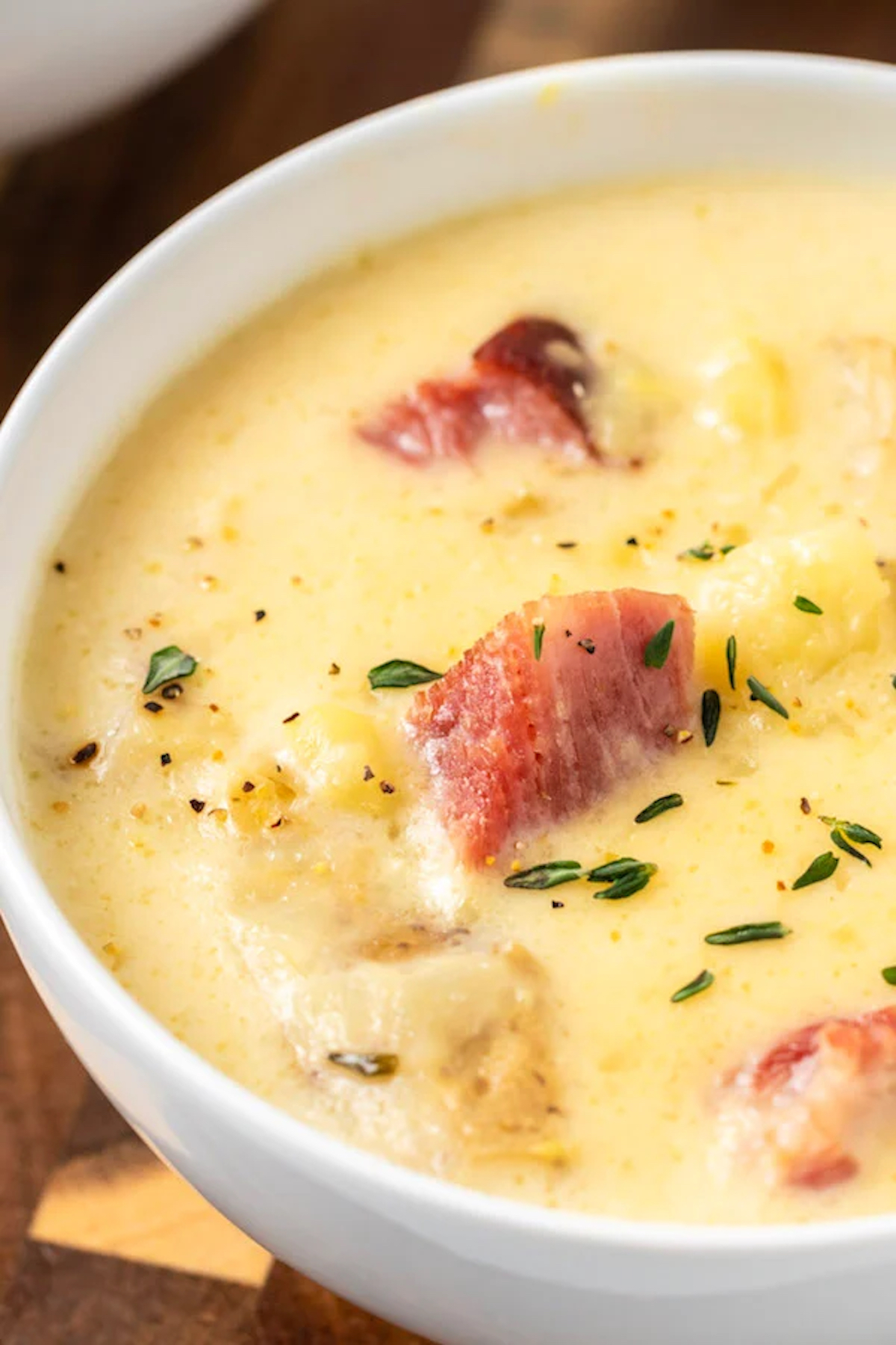 Close up of a white soup bowl filled with yellow, creamy Instant Pot soup with visible chunks of ham and potatoes.