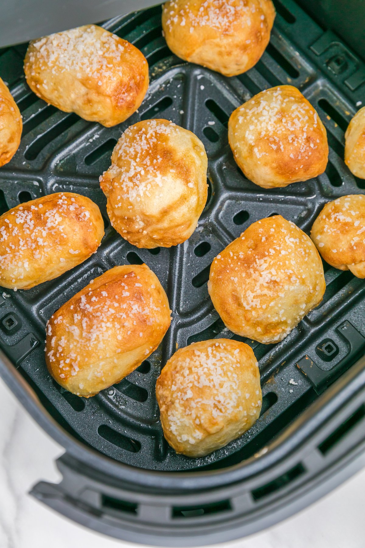 An air fryer basket with 11 cooked pretzel bites inside.