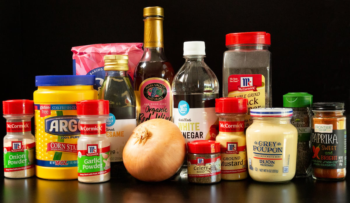 All the ingredients to make sweet onion sauce on a black background. Sugar, spice bottles, vinegar bottles, a sweet onion, mustard, and cornstarch.