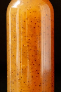 Close up of a glass bottle filled with brown subway sweet onion sauce. You can see the poppyseeds suspended throughout the sauce.