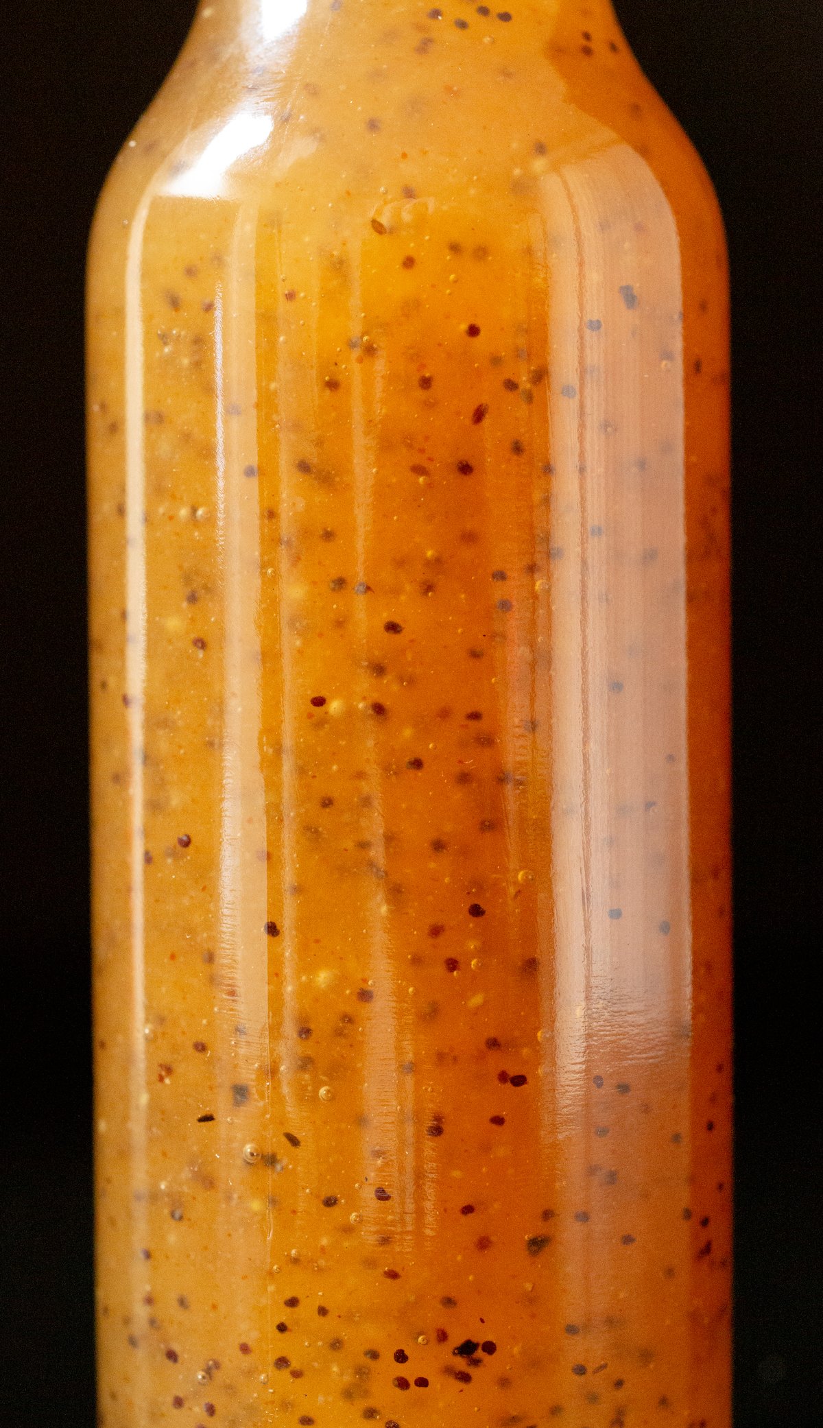 Close up of a glass bottle filled with brown subway sweet onion sauce. You can see the poppyseeds suspended throughout the sauce.